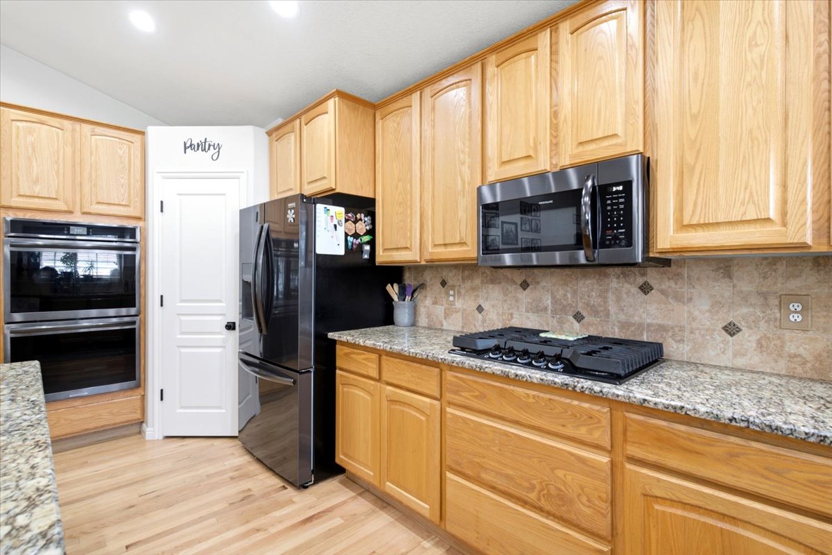 Kitchen featuring light wood cabinetry, granite countertops, a tiled backsplash, wood-finish flooring, and a double wall oven