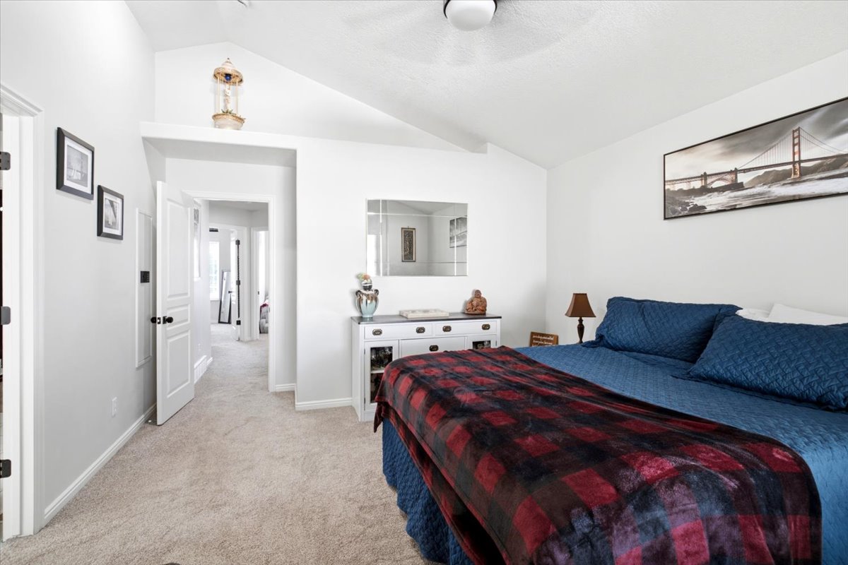 Vaulted ceiling Primary bedroom with light-toned carpet flooring and white painted walls