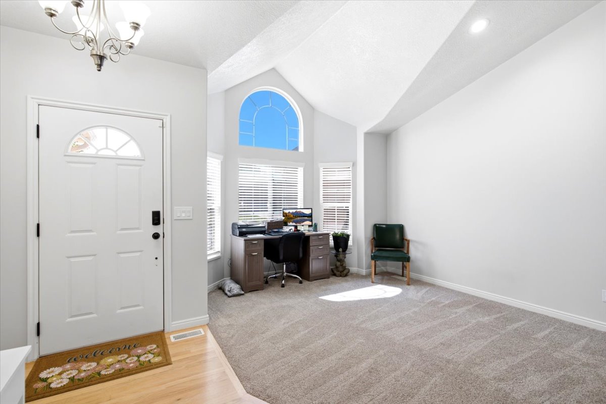 Vaulted ceiling entry, formal living room featuring a decorative chandelier and light wood-finish flooring