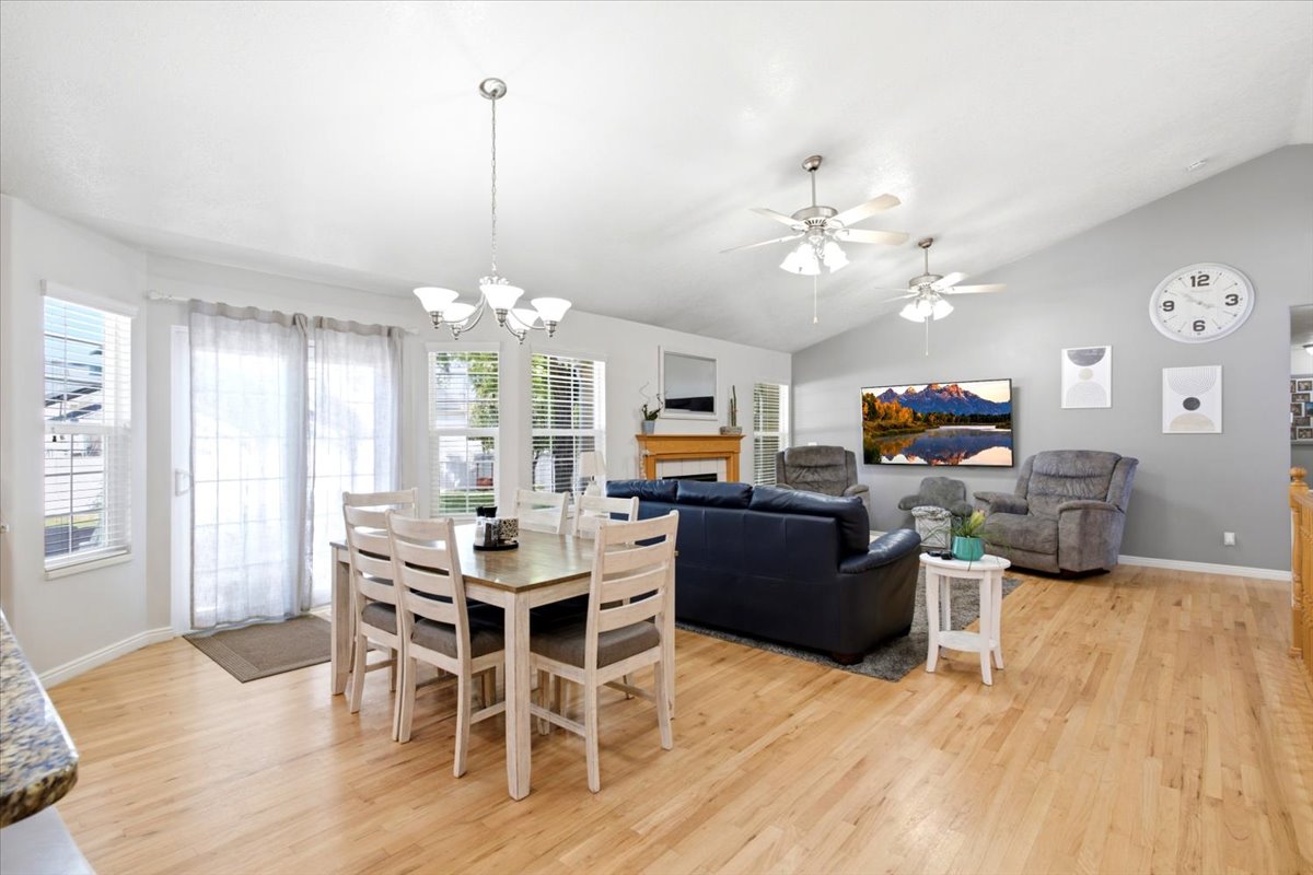 Vaulted ceiling great room featuring wood-finish flooring, multiple ceiling fans, and a fireplace with a wood mantle