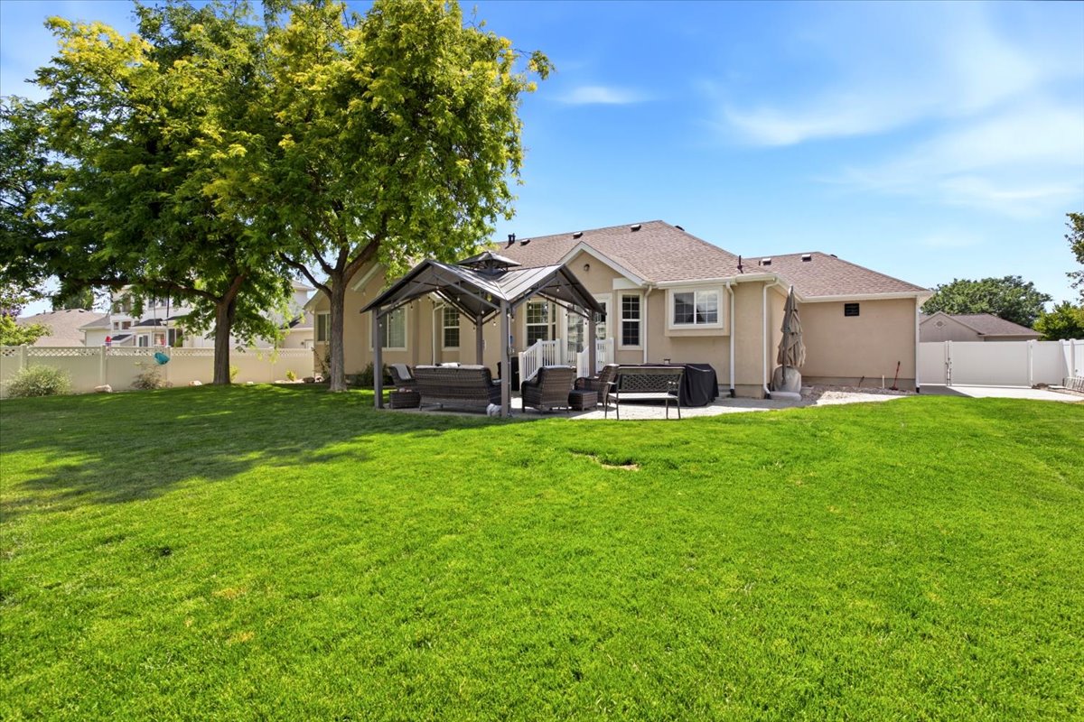 Expansive backyard featuring a large green lawn, two mature trees, and a concrete patio with gazebo.