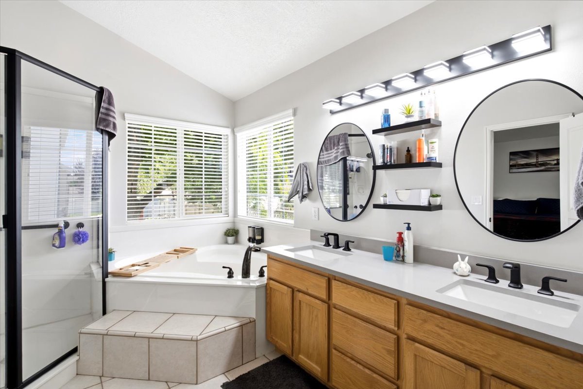 Spacious Primary bathroom featuring a double vanity with quartz countertops, a built-in jetted soaking tub, a glass-enclosed shower, and multiple windows