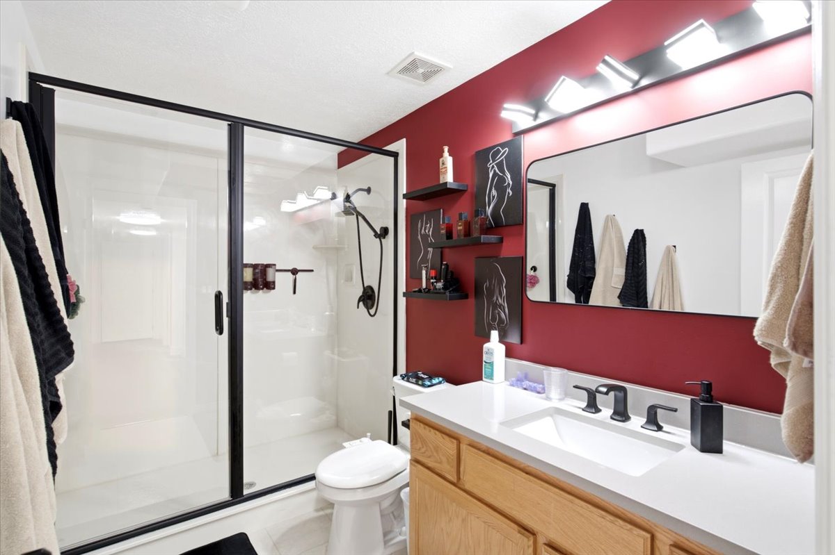 Contemporary bathroom featuring a walk-in shower with black-framed glass enclosure, light wood-finish vanity with an integrated sink, polished countertop, and a vanity mirror with overhead lighting