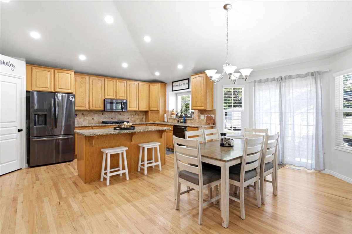 Open concept kitchen and dining area featuring wood-finish flooring, light wood cabinetry, granite stone countertops, stainless steel appliances, and a built-in kitchen island with seating