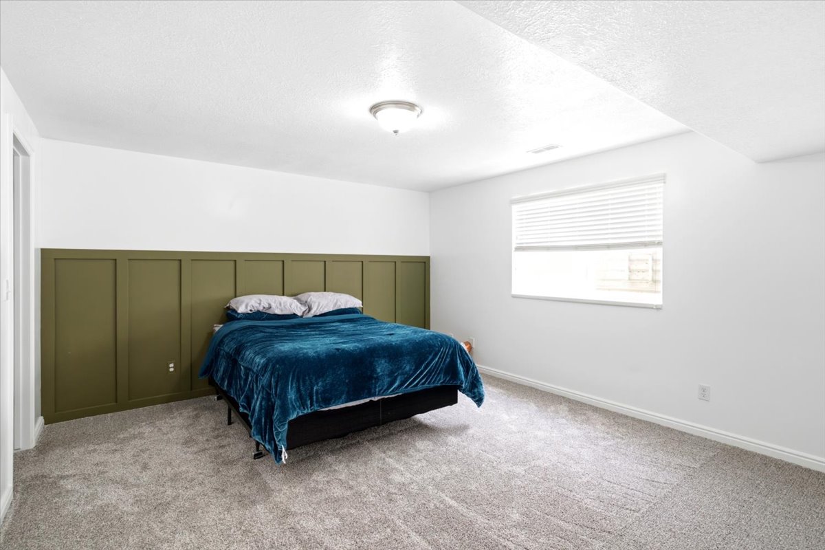 Spacious room featuring board and batten wall detailing, neutral carpeting, a single window with blinds, and an overhead flush-mount light fixture