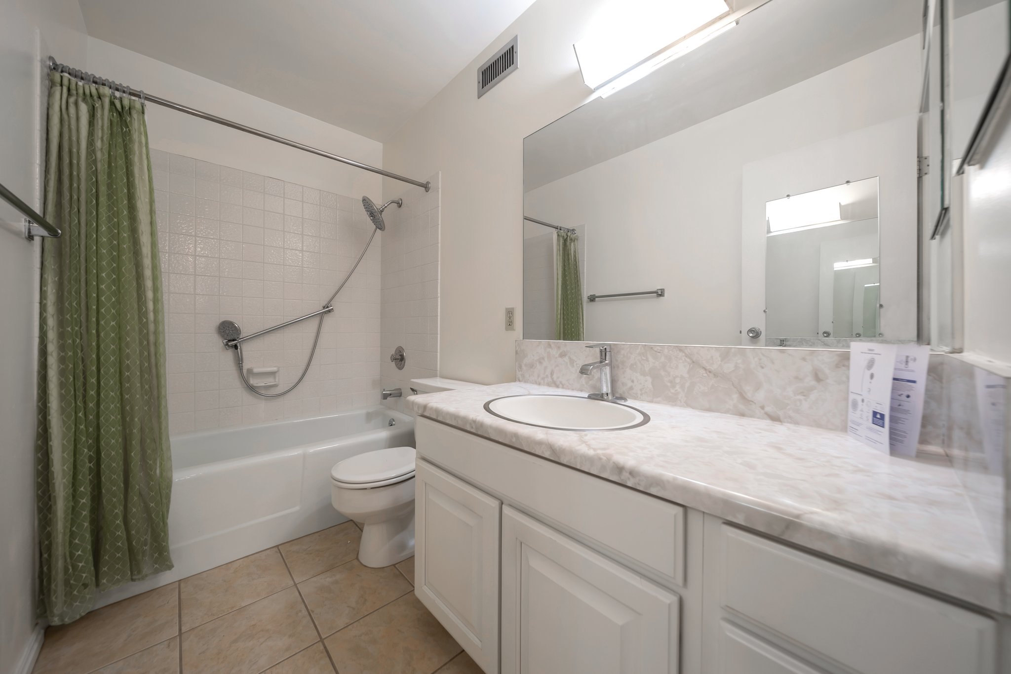 Bathroom featuring a white vanity with an integrated sink, a large mirror, and a full-size bathtub with a shower