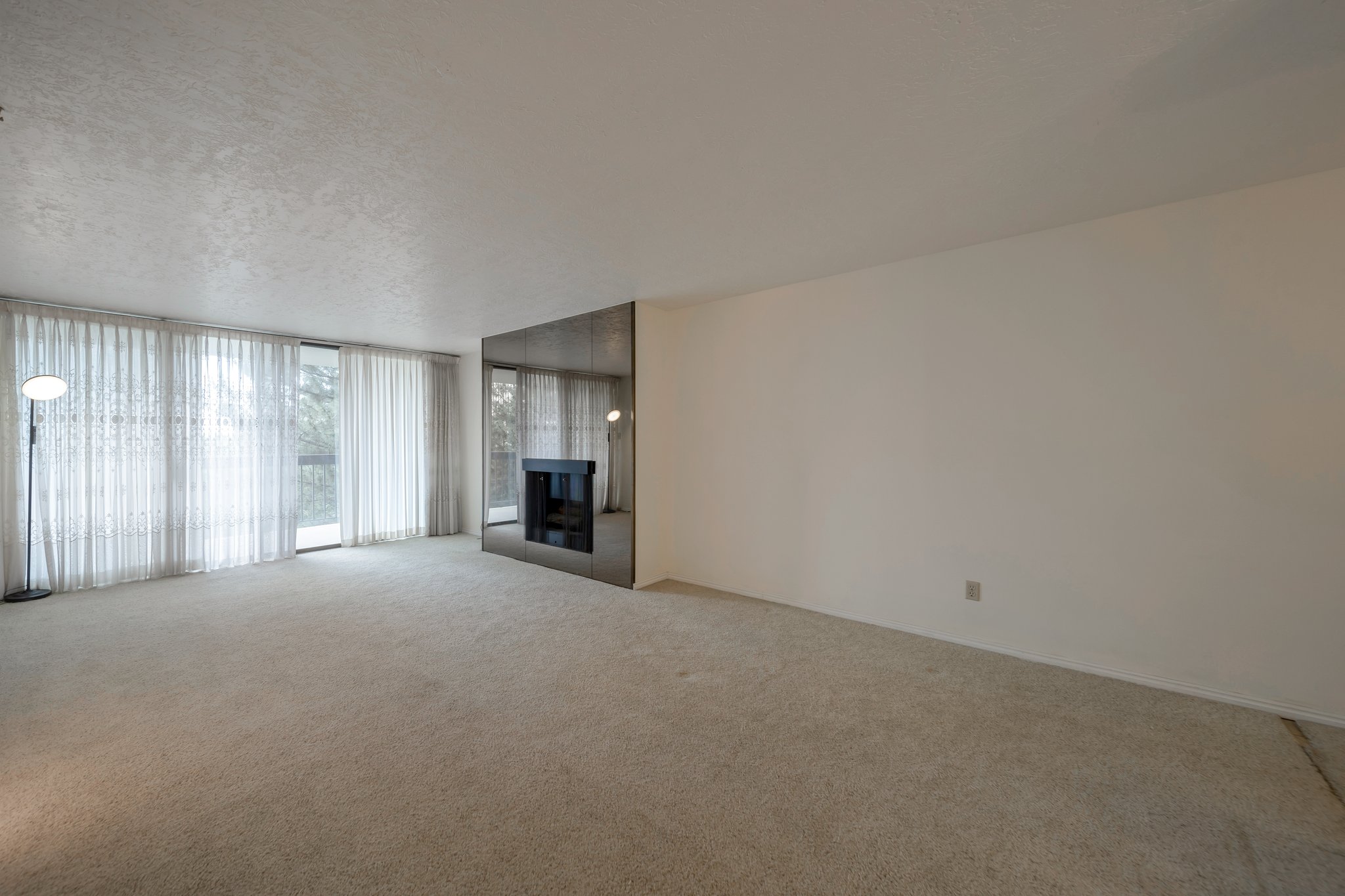 Spacious living area featuring light-toned carpeting and a mirrored accent wall with a built-in fireplace