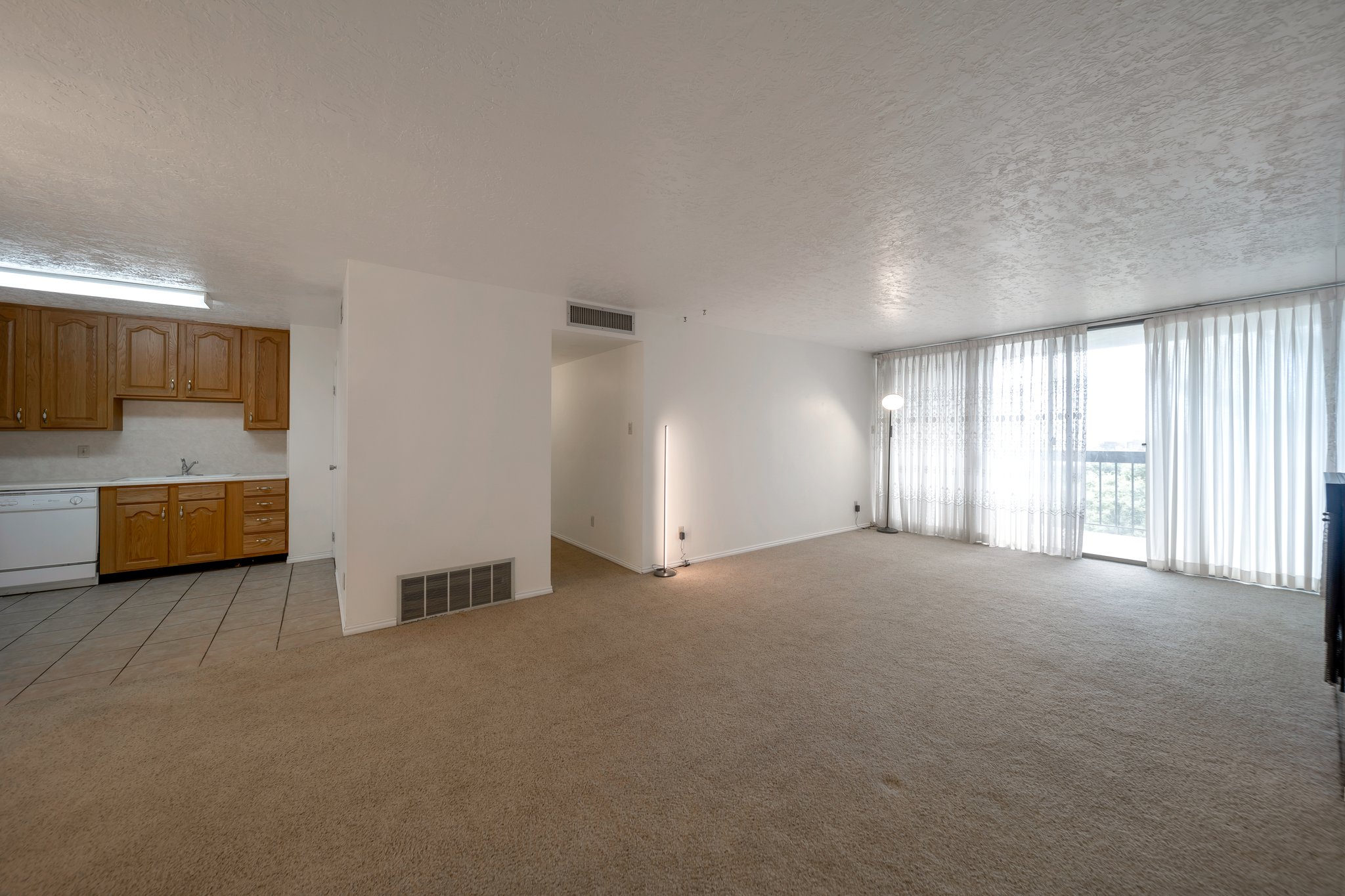 Spacious living area with carpet flooring, large sliding glass doors, and vertical blinds