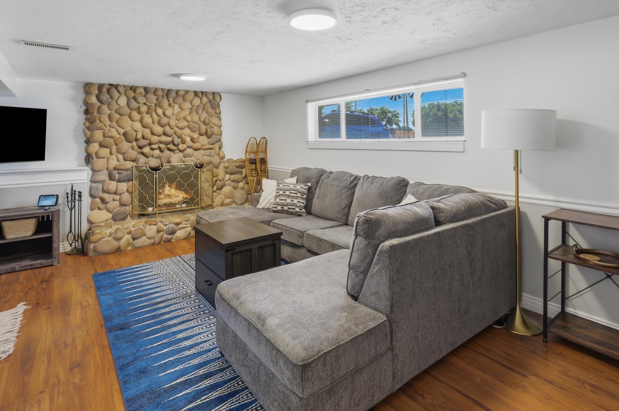 Living area featuring a floor-to-ceiling river rock fireplace with a brass screen, wood-finish flooring, and white baseboards