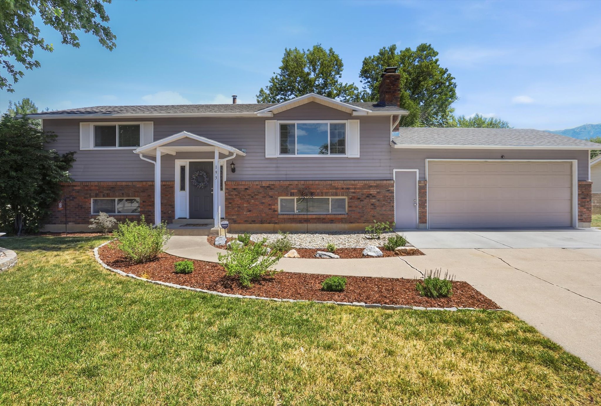 Split-level residence featuring a two-car garage, brick and siding exterior, covered entry, and concrete driveway