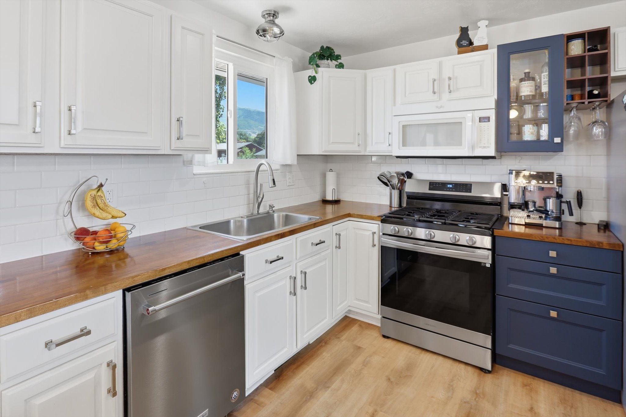 Modern kitchen featuring white shaker cabinetry, wood-finish countertops, and stainless steel appliances