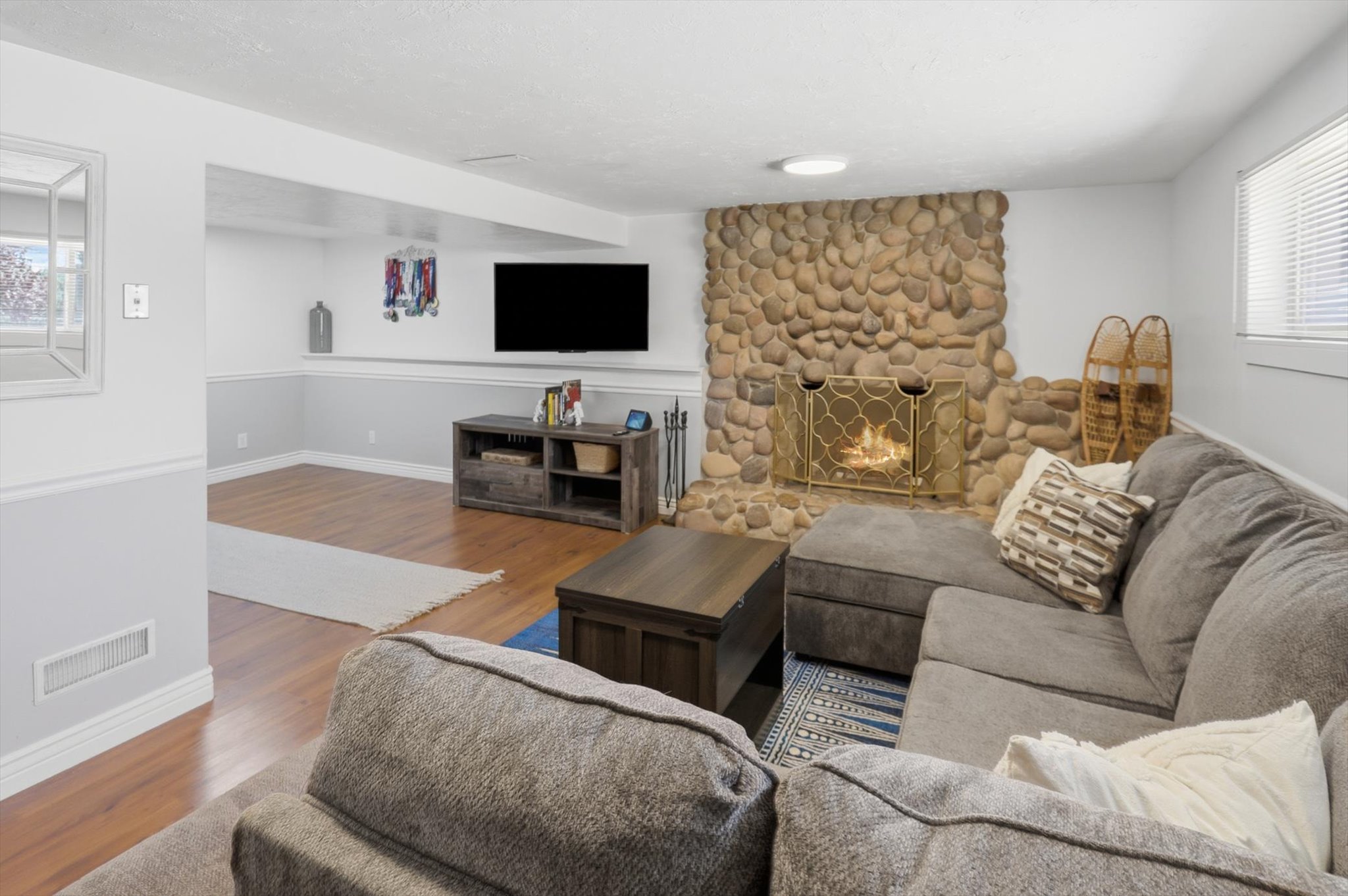 Stone-clad fireplace featuring a brass screen, wood-finish flooring, white baseboards, and a window with blinds