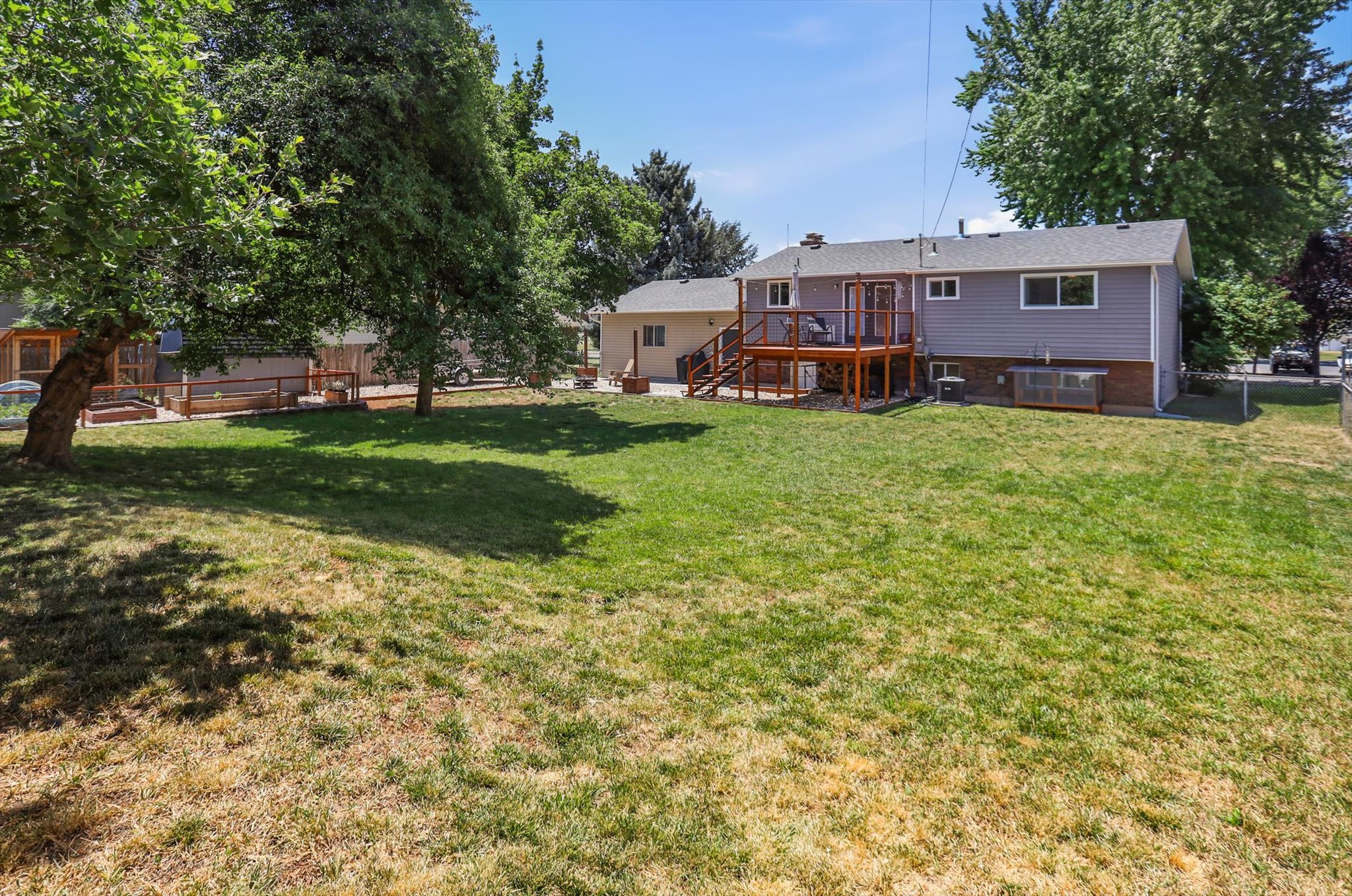 Spacious backyard featuring a multi-level wooden deck, mature trees, and a separate fenced area