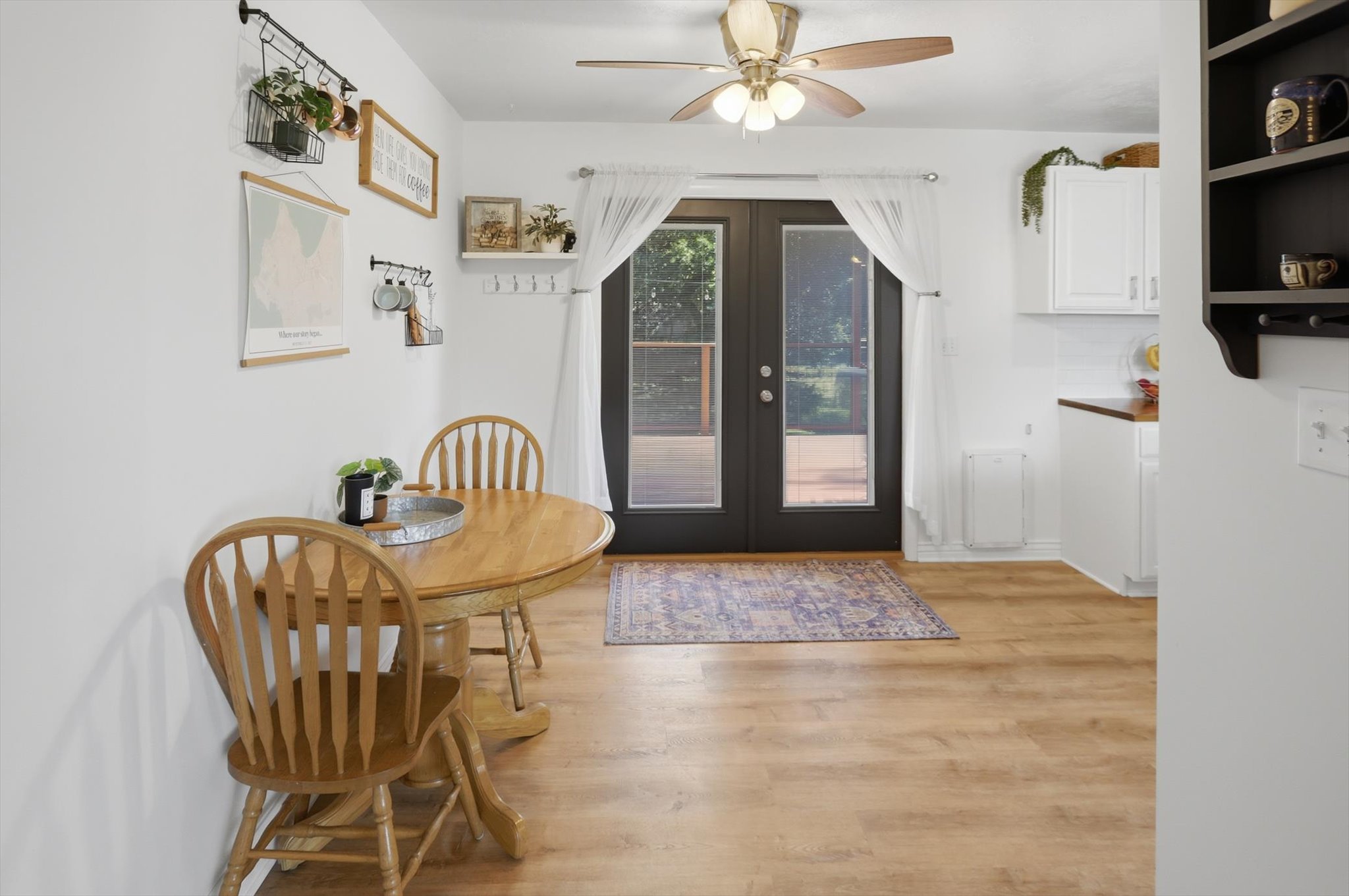 Patio doors with dark trim open to an outdoor area, complemented by wood-finish flooring and a ceiling fan with light fixture
