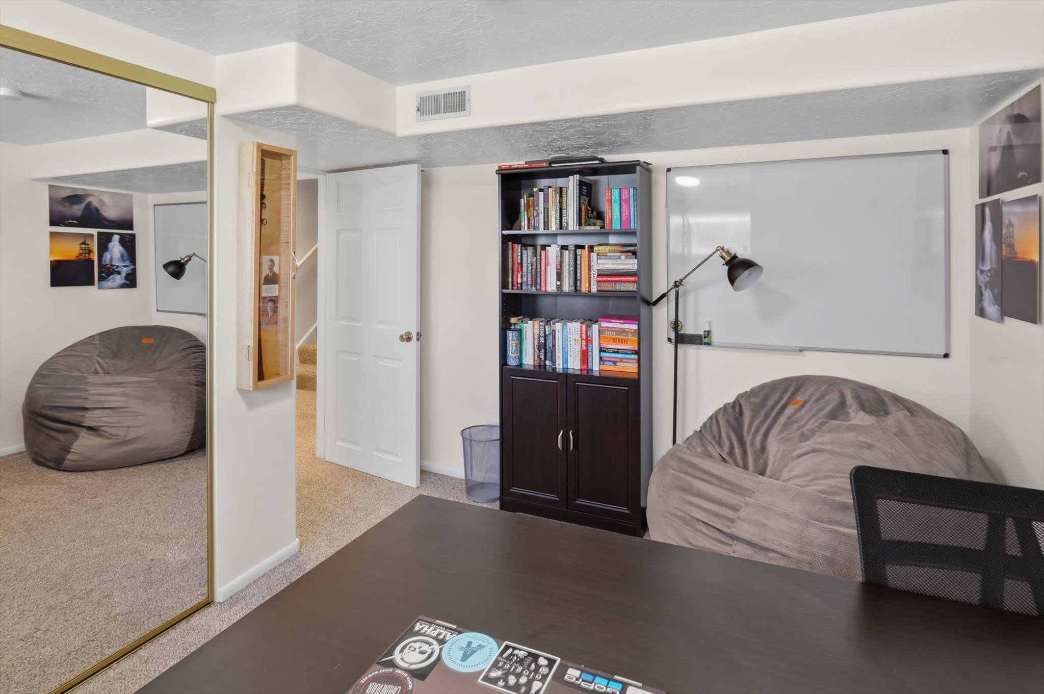 Carpeted interior space featuring a built-in bookshelf, overhead lighting, and a wall-mounted whiteboard