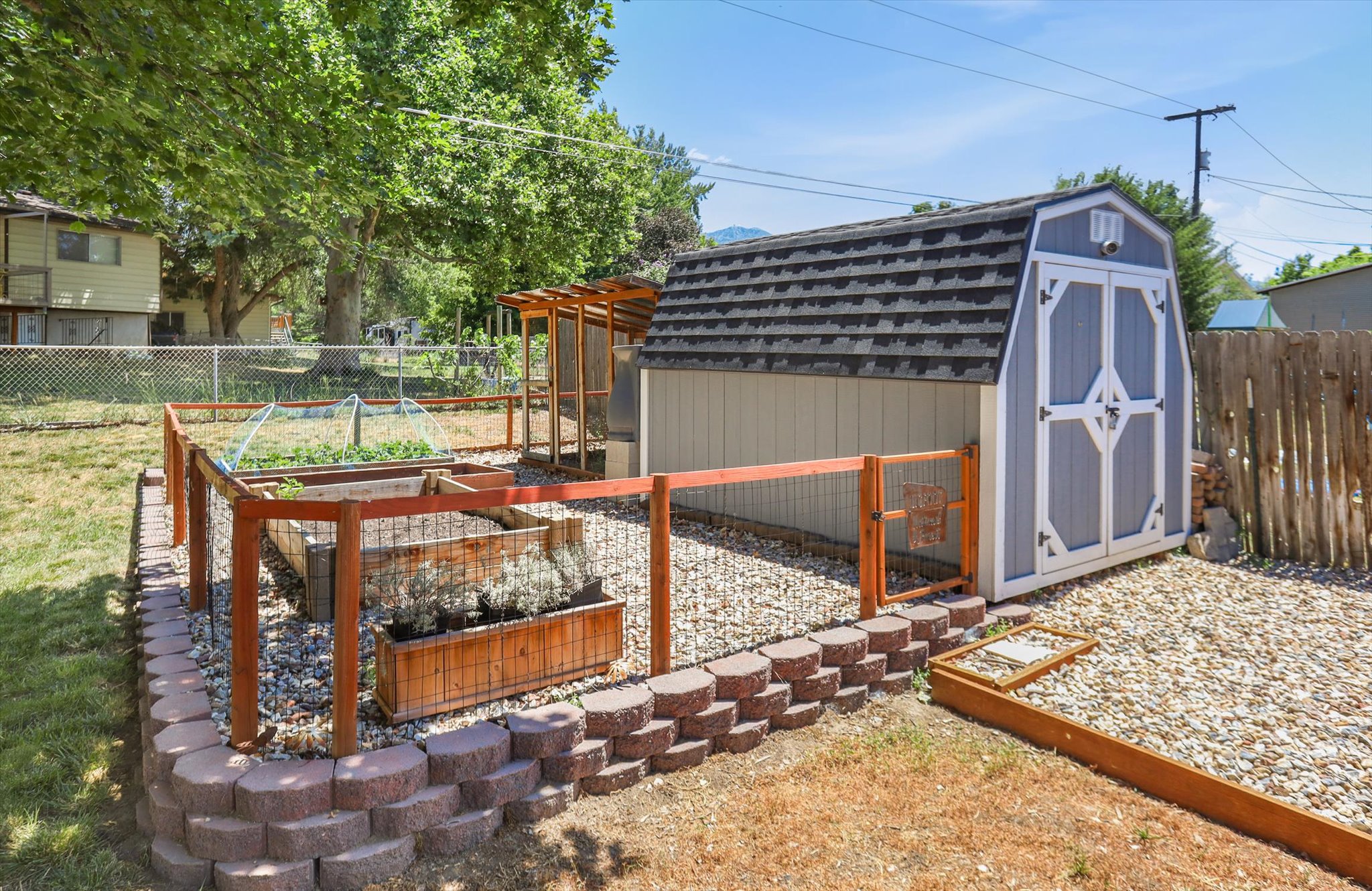 Backyard featuring a gambrel-roof storage shed, fenced raised garden beds, a terraced retaining wall, and a gravel area