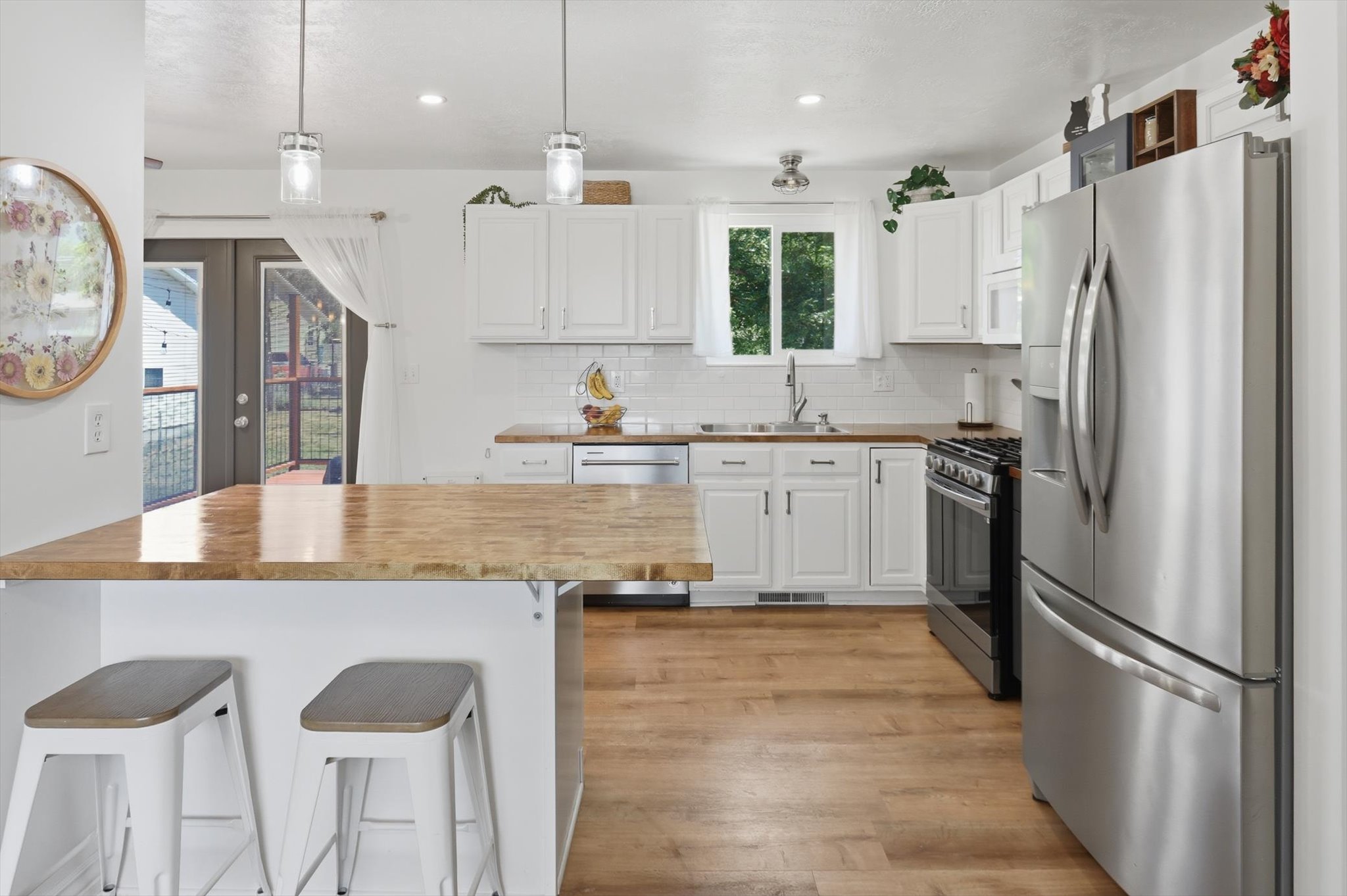 Open-concept kitchen featuring wood-finish flooring, white cabinetry, a wood-finish island countertop, and stainless steel appliances