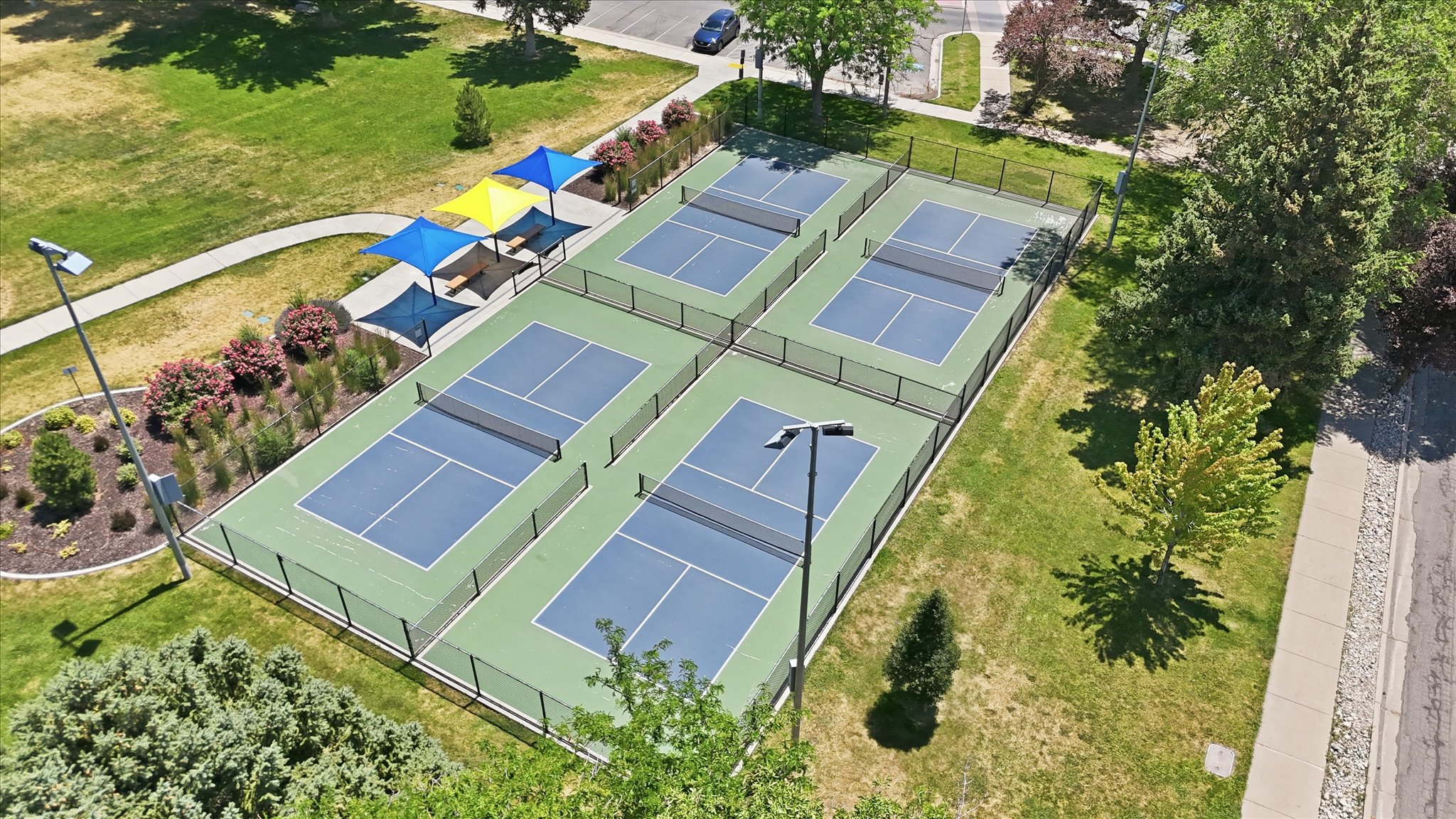 Four fenced pickleball courts featuring blue and green playing surfaces