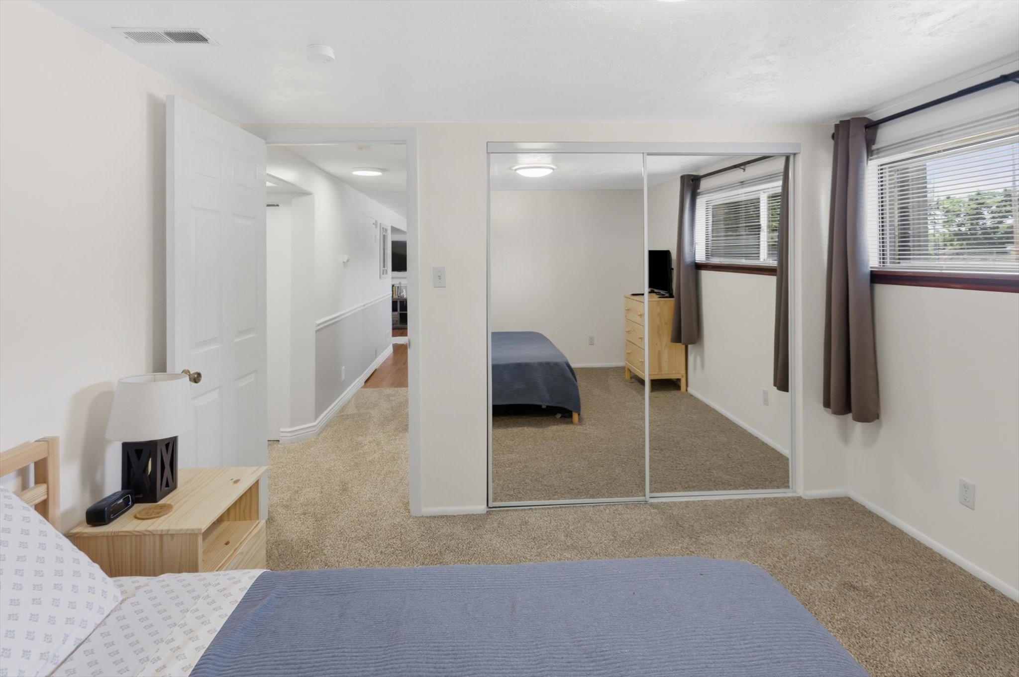 Carpeted room featuring a full-wall mirrored closet, two windows with blinds, and white painted walls