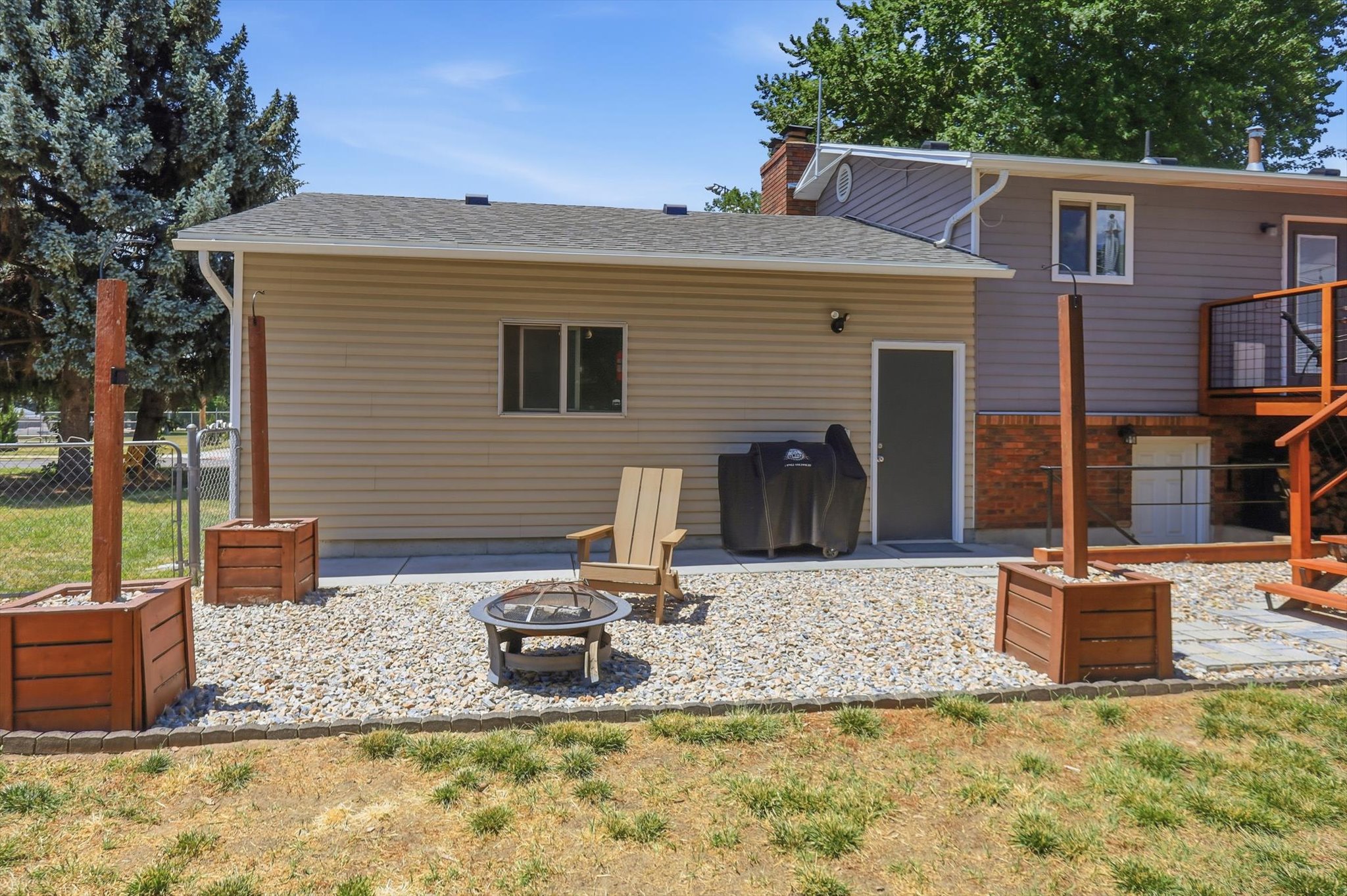 Expansive gravel patio featuring a built-in fire pit, stone paver accents, and two large wooden planters