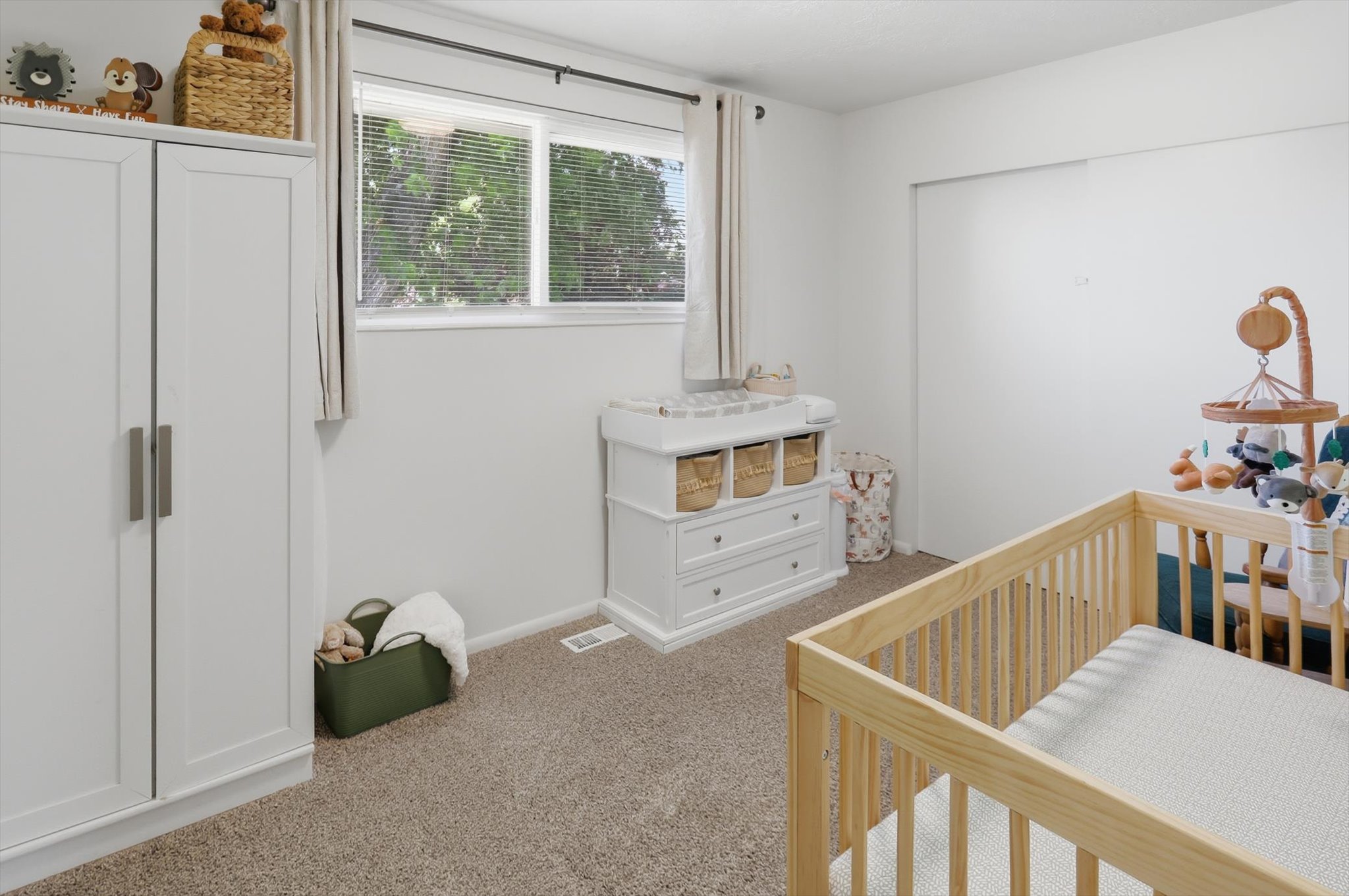 Carpeted interior space featuring a window with blinds, white walls, and a recessed closet with sliding doors