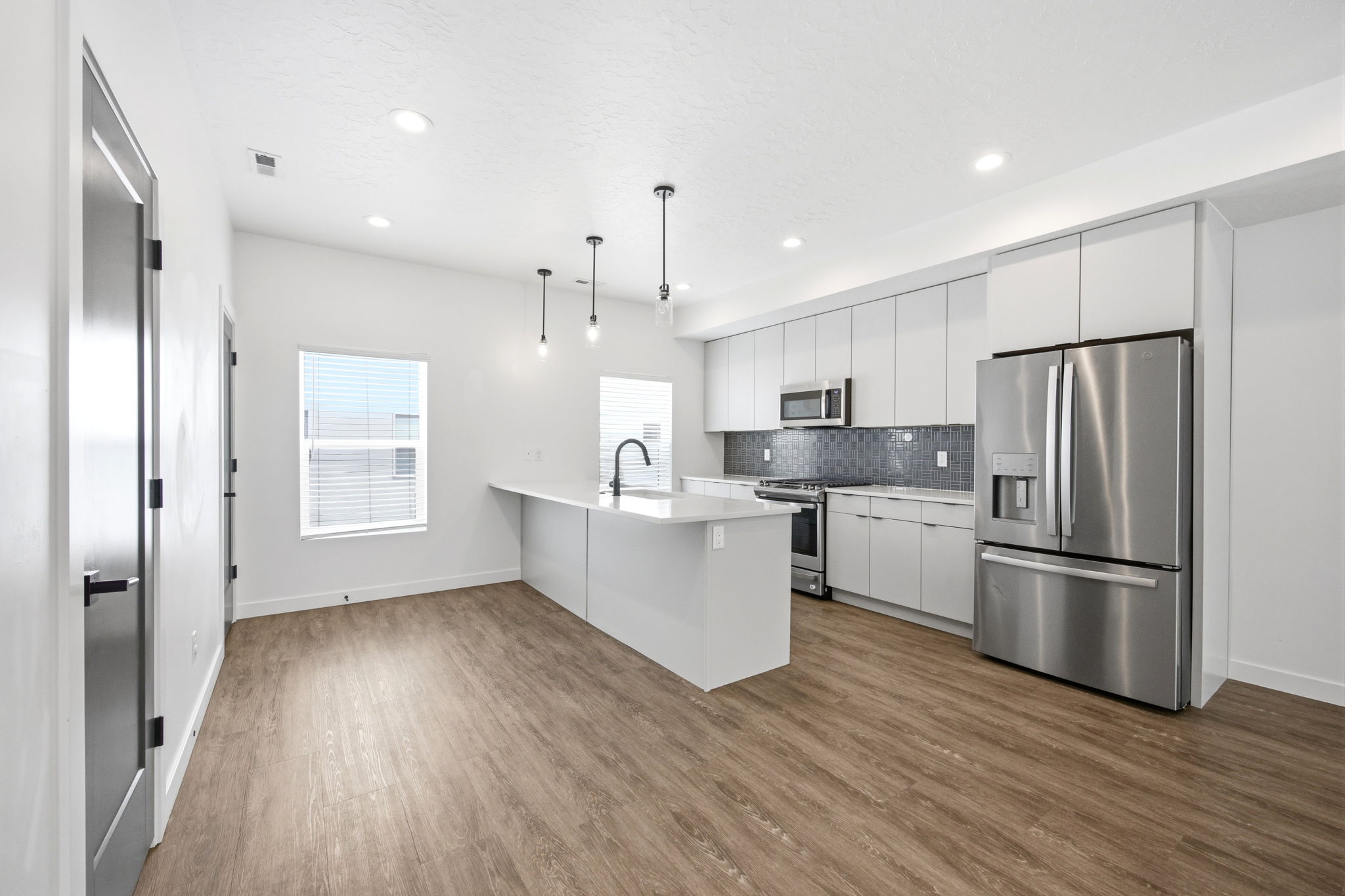 Contemporary kitchen featuring stainless steel appliances, white flat-panel cabinetry, a dark mosaic tile backsplash, and light wood-finish flooring