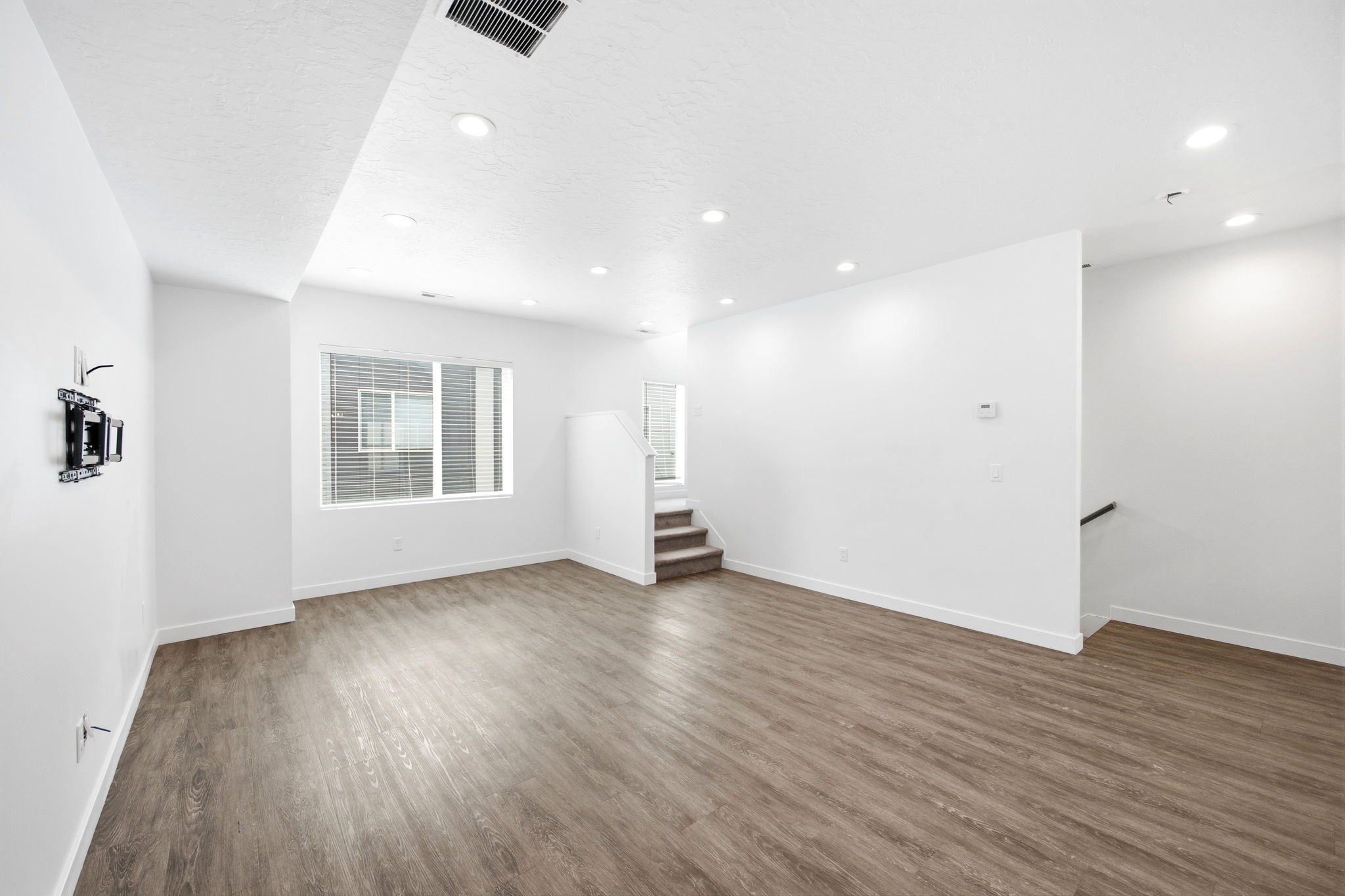 Spacious interior with wood-finish flooring, recessed lighting, white walls, and a window with blinds