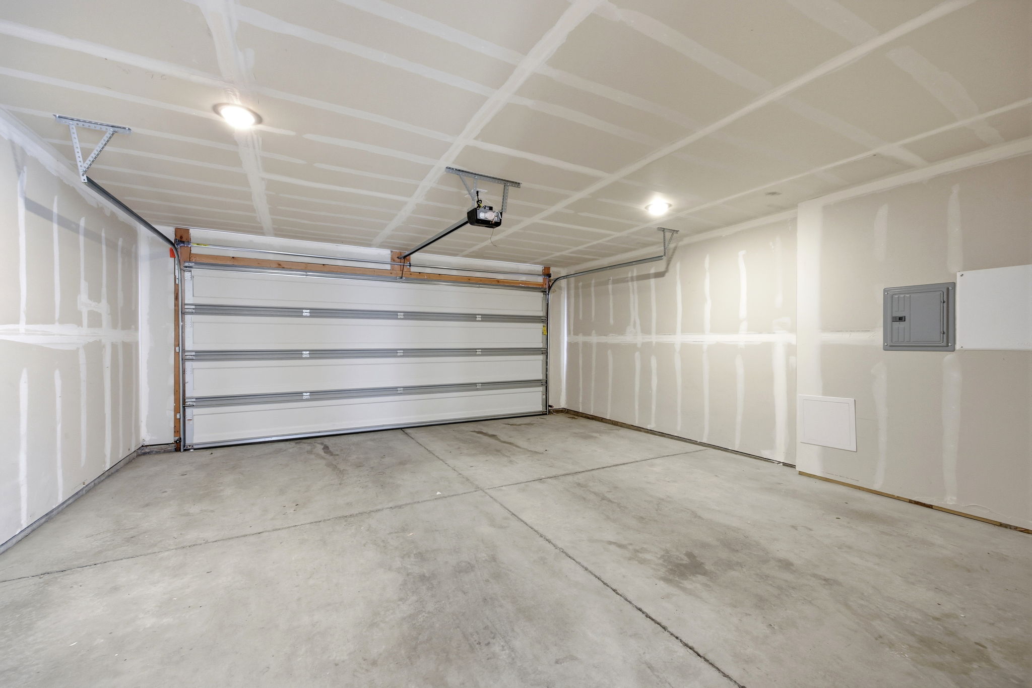 Spacious garage featuring a concrete floor, overhead lighting, an automatic garage door opener, and a wall-mounted electrical panel