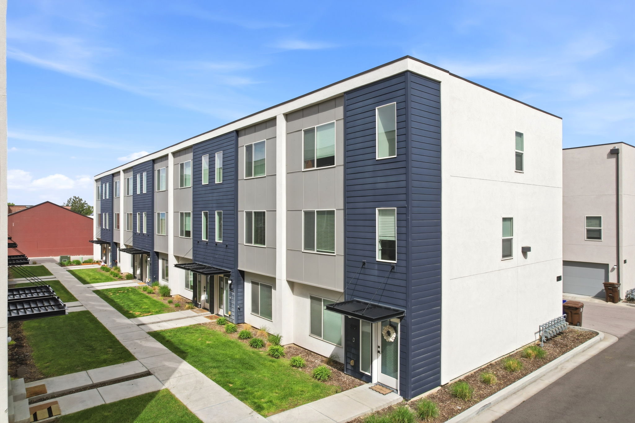 Modern townhome exterior featuring a three-story design, a contrasting facade of white stucco and dark blue siding, and a covered entry