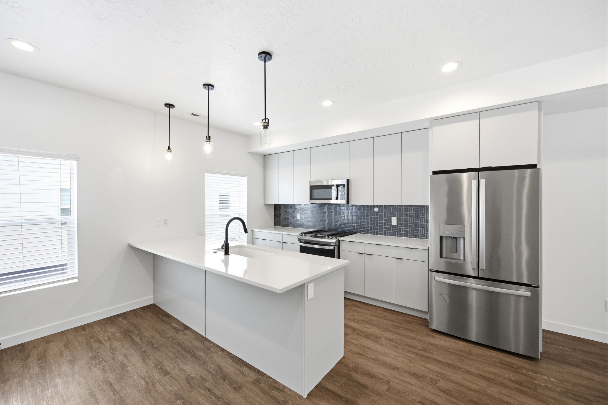 Contemporary kitchen featuring a large island with sink, stainless steel appliances, white flat-panel cabinetry, a dark tile backsplash, and wood-finish flooring