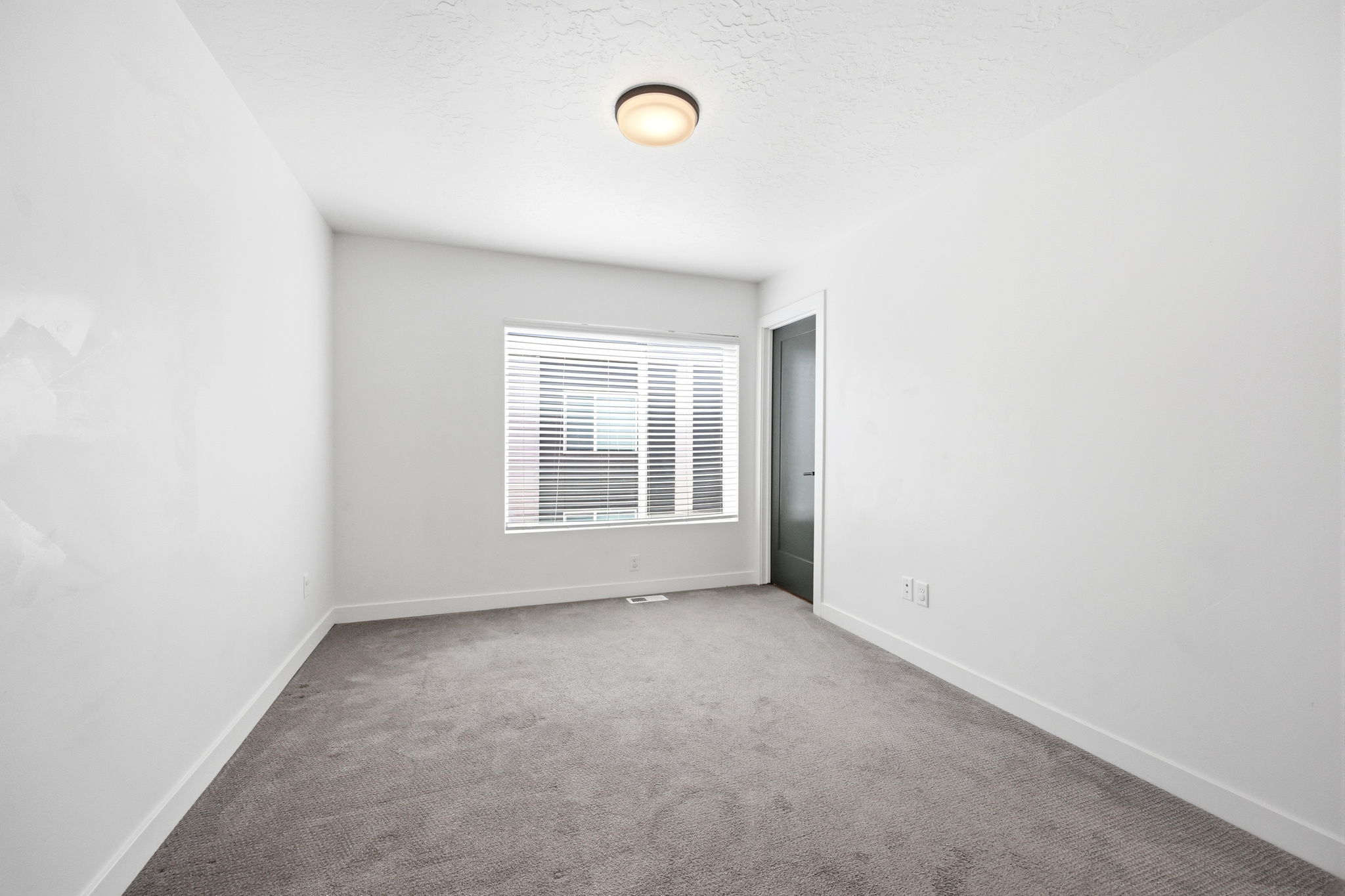 Carpeted interior space featuring a window with blinds, white walls, and a contemporary flush-mount ceiling light