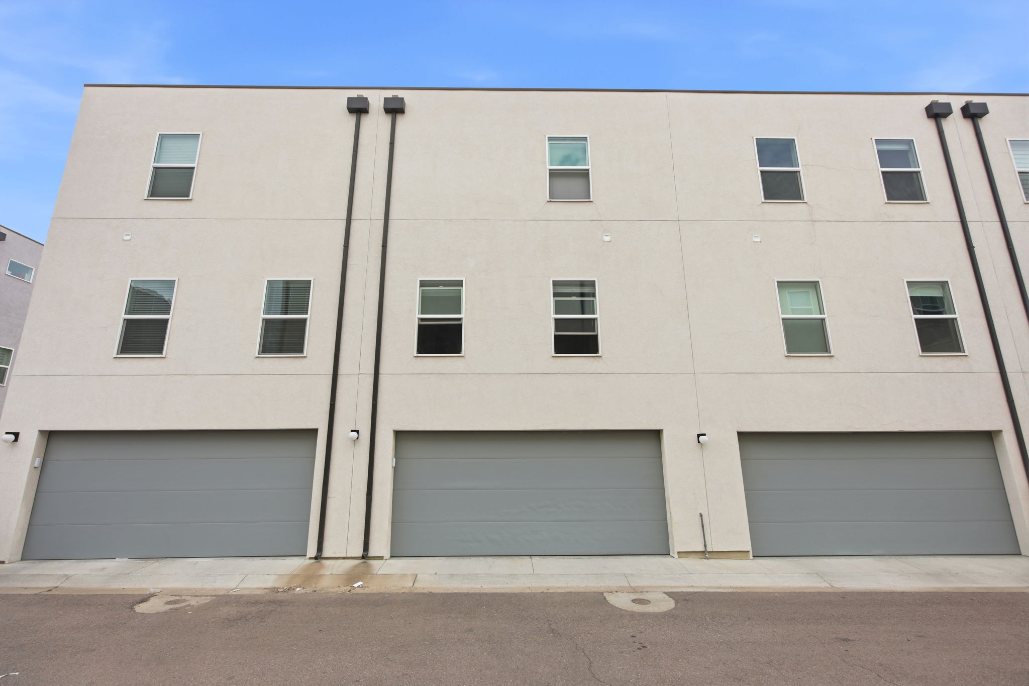 Multi-level exterior featuring stucco siding, three integrated garage doors, multiple window installations, and exterior lighting fixtures