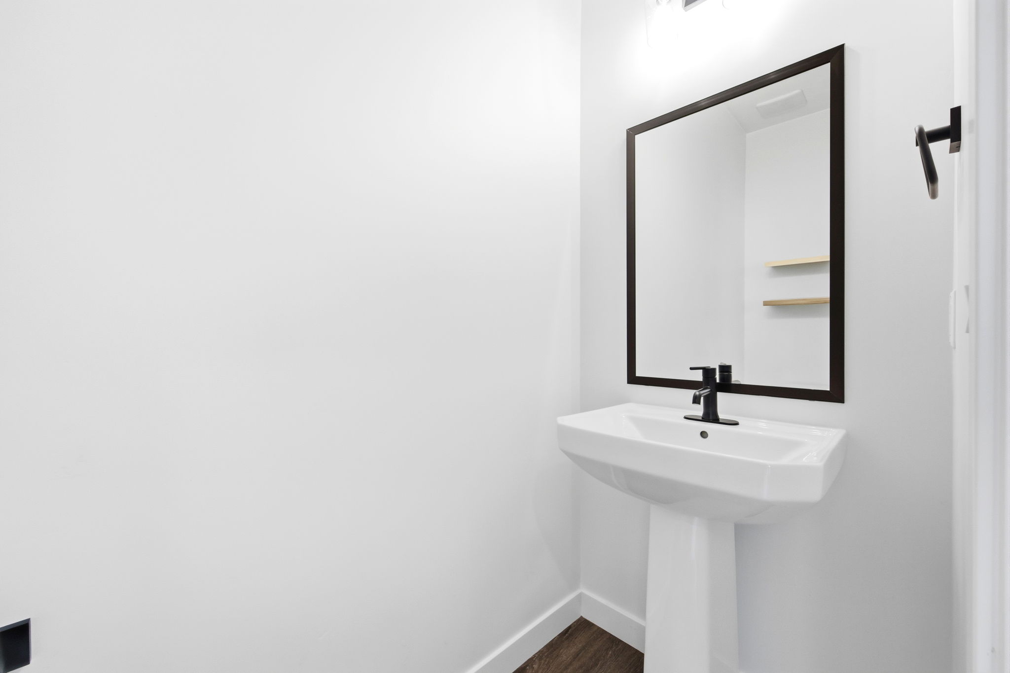 Pedestal sink with matte black faucet, framed mirror, and integrated lighting