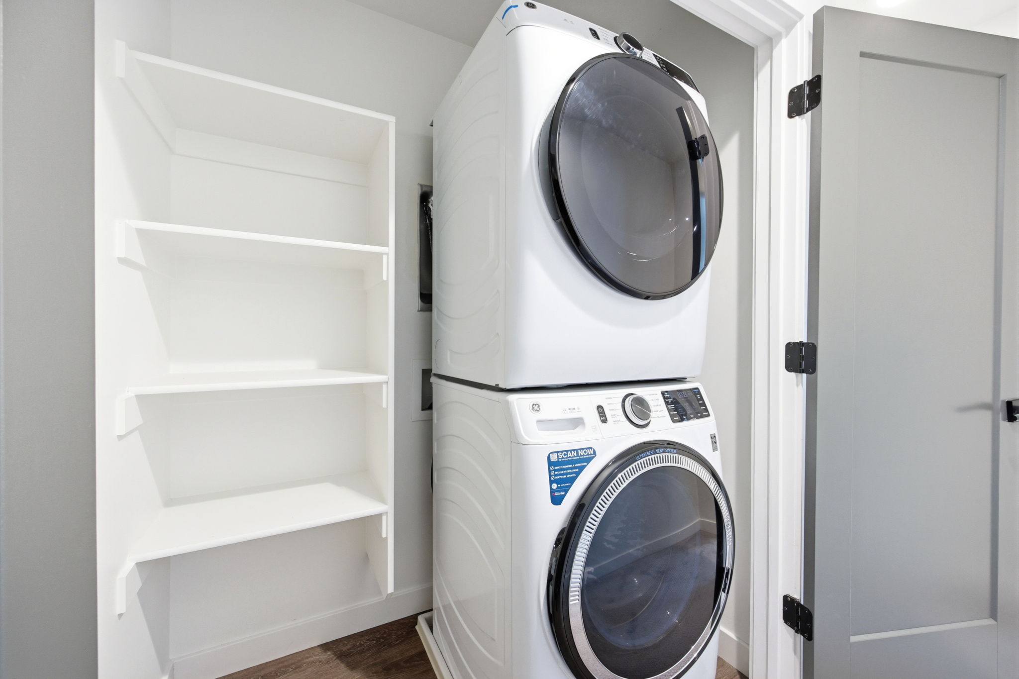 Laundry area featuring a stackable washer and dryer, adjacent built-in shelving, white baseboards, and wood-finish flooring