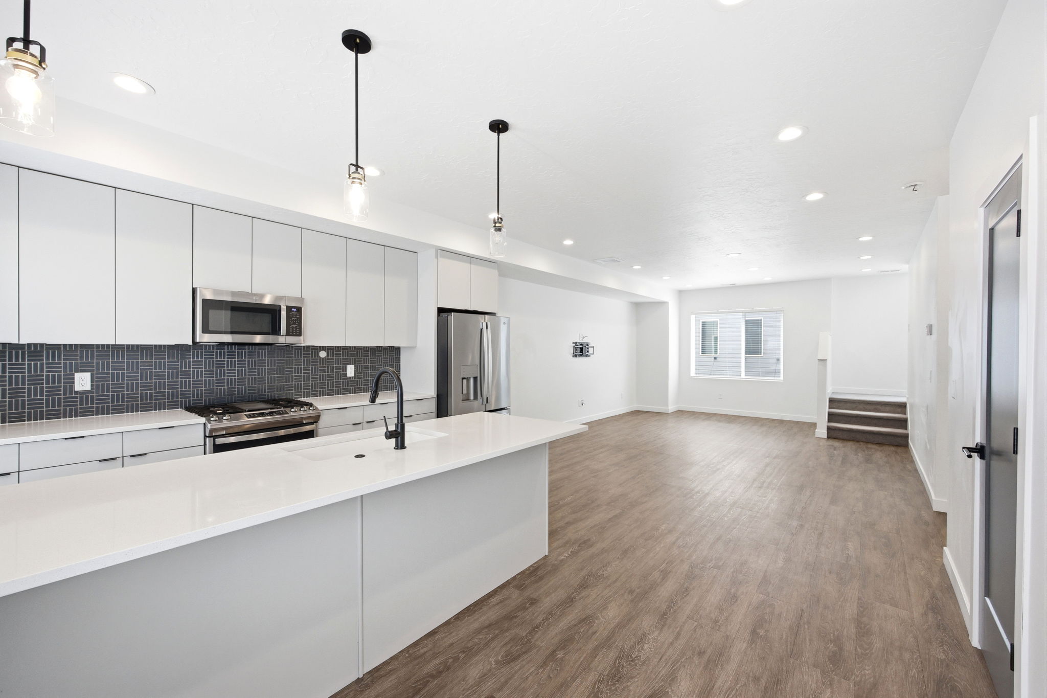 Modern kitchen featuring a large island with white countertops, sleek gray cabinetry, stainless steel appliances, and a dark mosaic tile backsplash