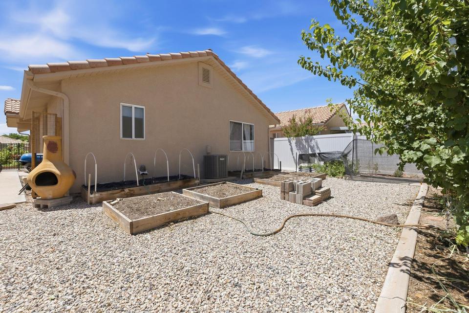 Rear exterior featuring stucco siding, a terracotta tile roof, and multiple raised garden beds