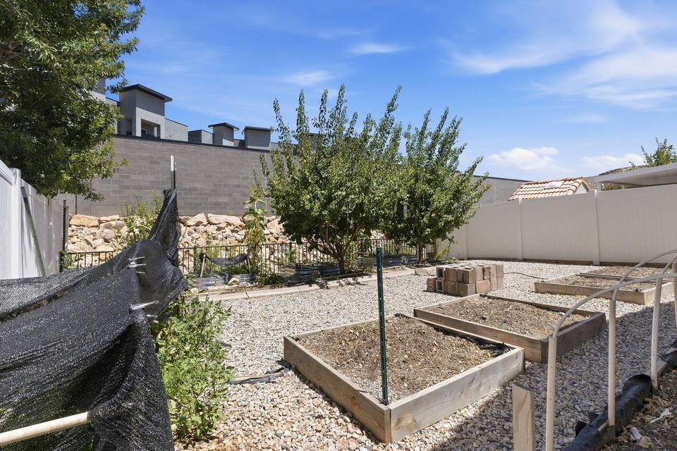 Expansive backyard featuring gravel landscaping, multiple raised garden beds, mature trees, and a privacy fence