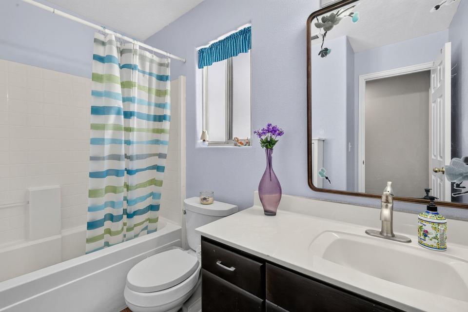 Bathroom with a white tub and shower combination, a dark wood-finish vanity with an integrated white sink, a chrome faucet, and a wall-mounted mirror