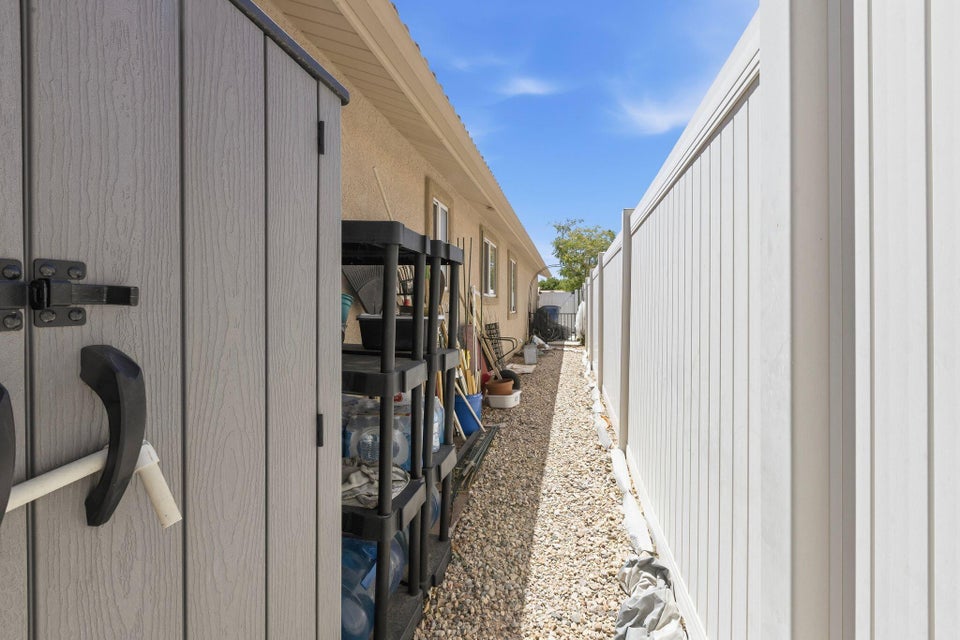 Gravel-lined side yard featuring a durable white privacy fence and a textured storage shed