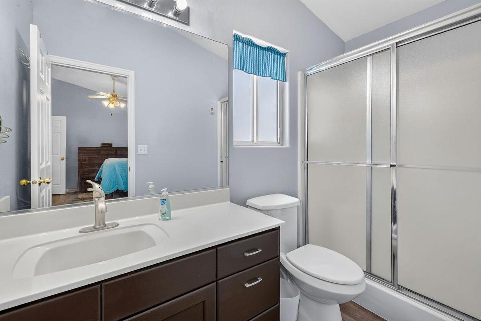 Bathroom featuring a dark wood-finish vanity with a white integrated sink, a large wall-mounted mirror, a toilet, and a shower with frosted sliding doors