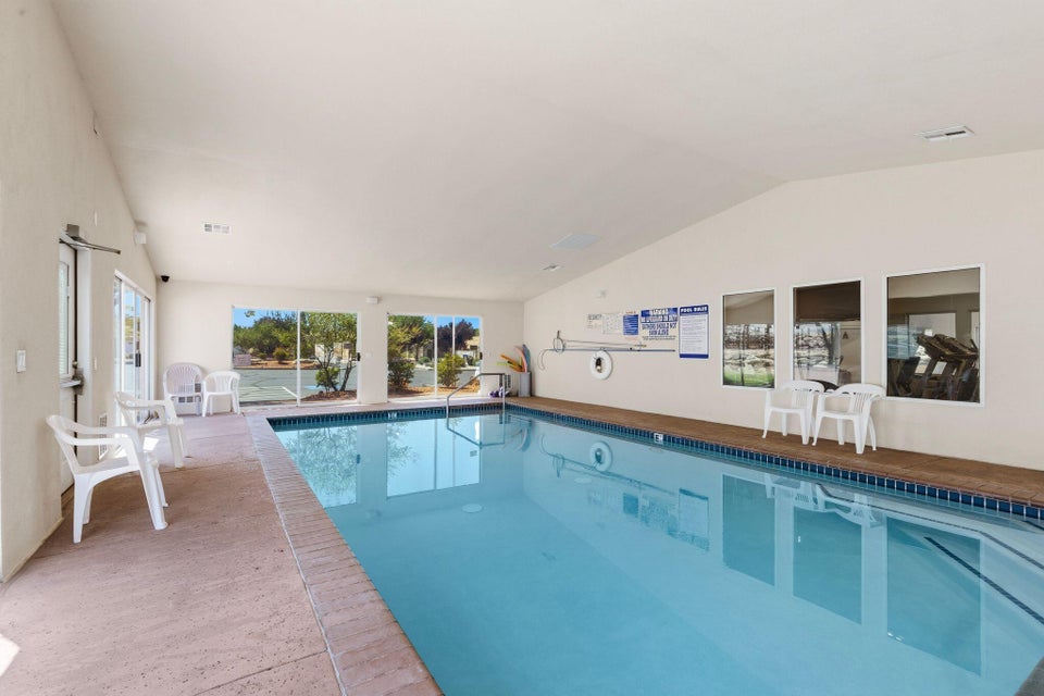 Indoor swimming pool with concrete decking, large windows, and a vaulted ceiling