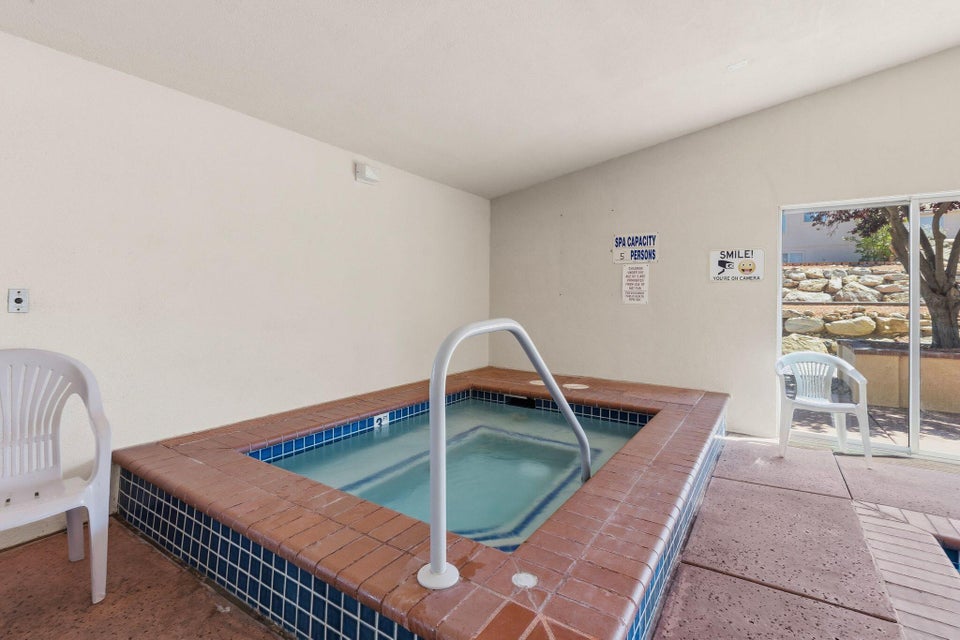 Indoor spa with blue and brown tile surround, white grab rail, and concrete flooring