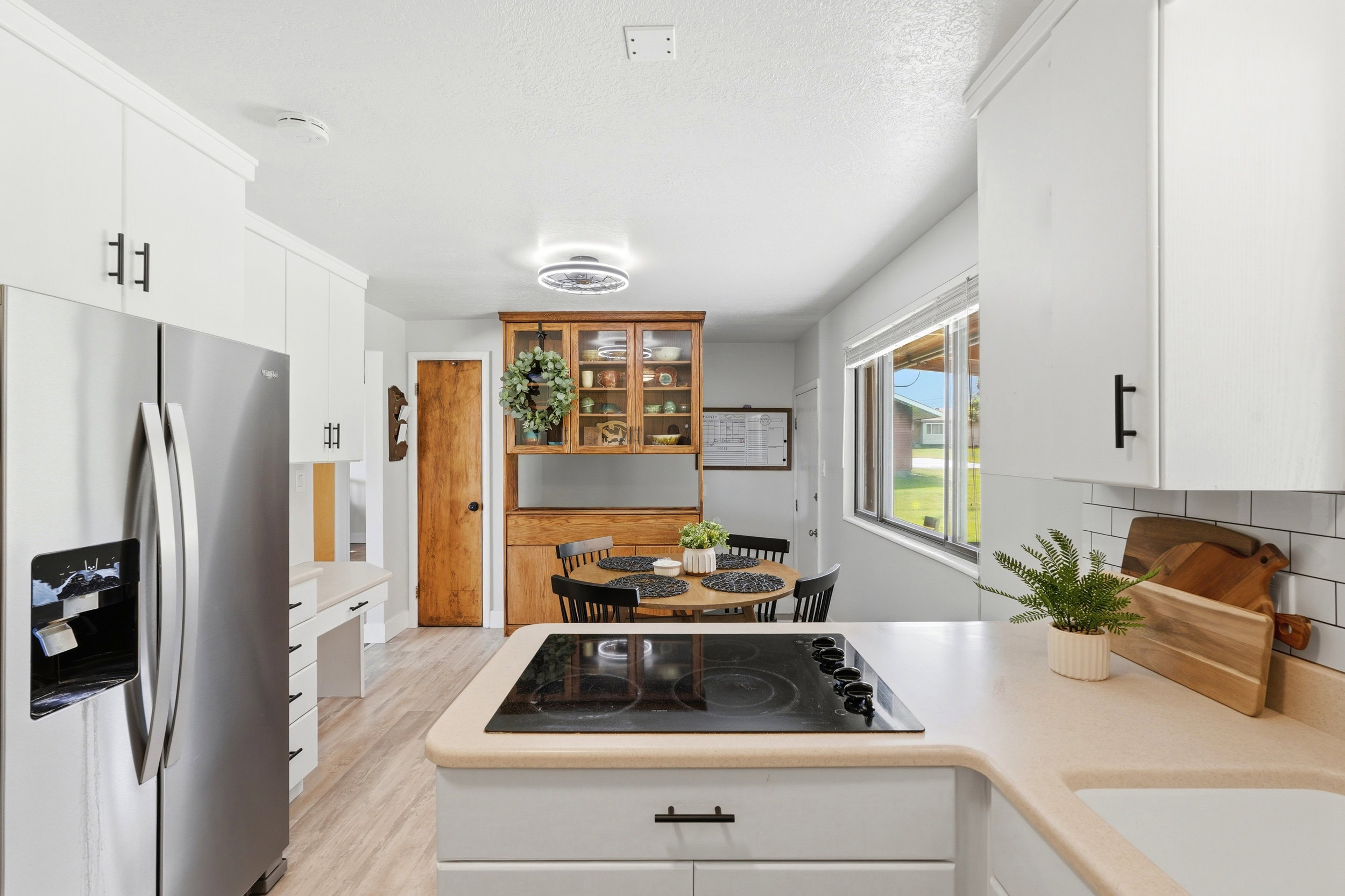 Kitchen featuring white cabinetry with black hardware, stainless steel refrigerator, electric cooktop, light-toned countertops, and wood-finish flooring
