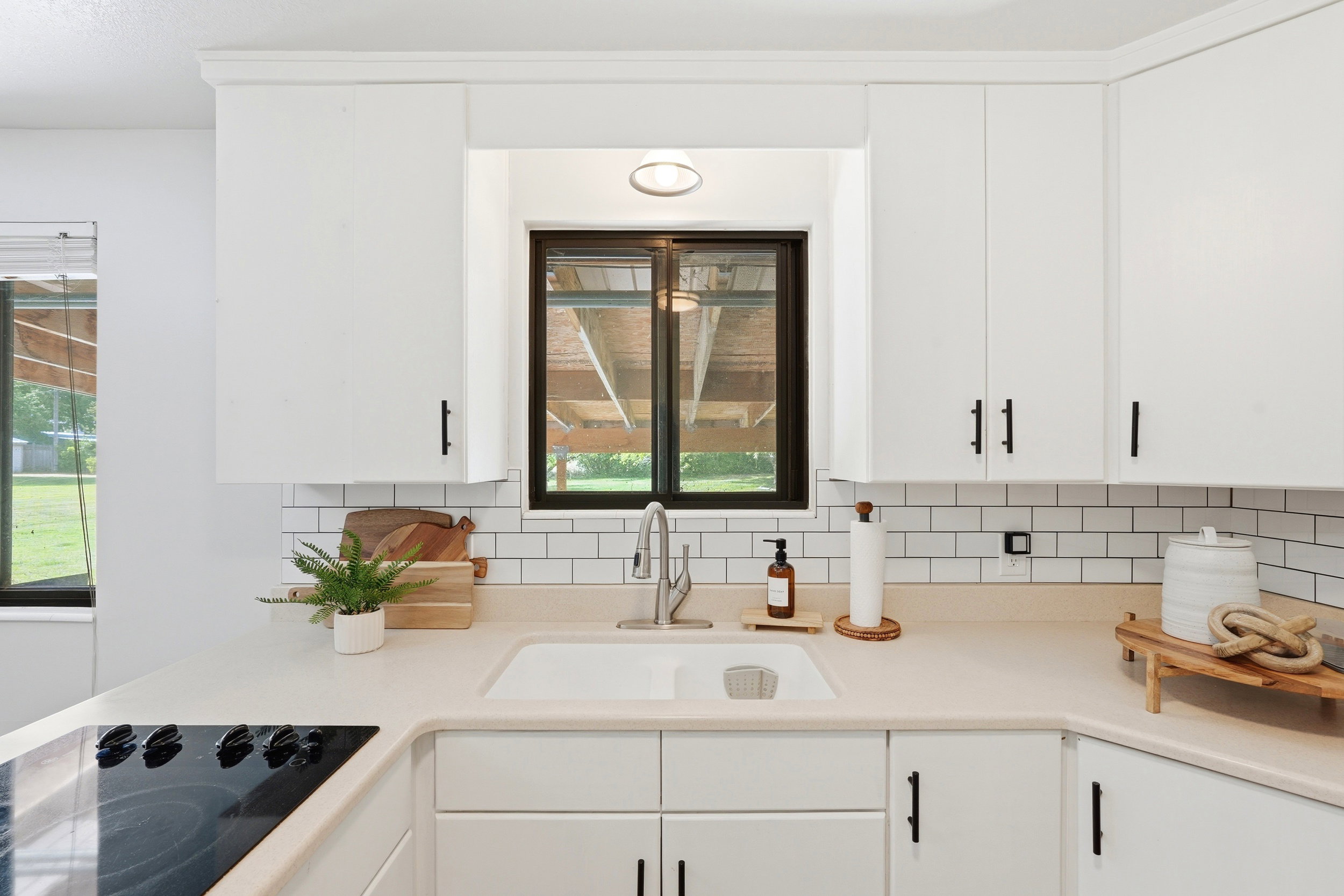 Modern kitchen featuring white cabinetry, light-toned countertops, a subway tile backsplash, and a built-in cooktop