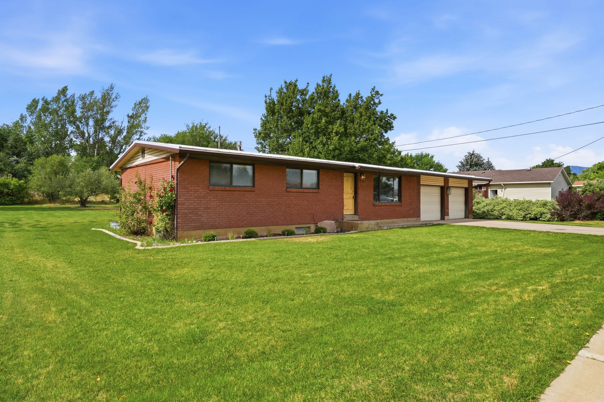 Brick exterior residence featuring a two-car garage, mature front lawn, and foundational plantings