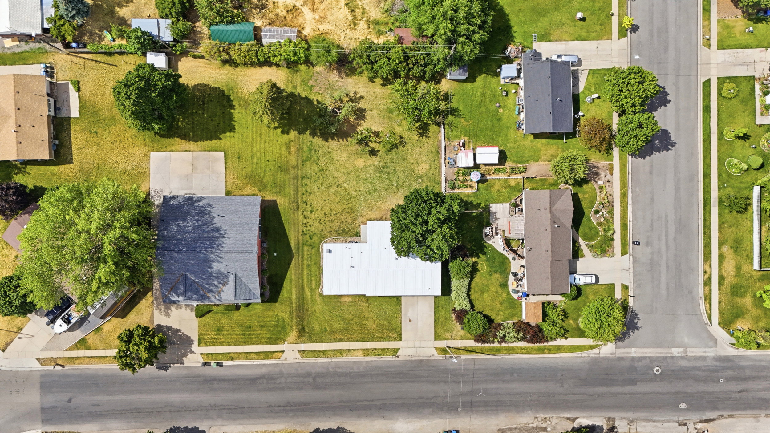 Aerial property perspective featuring a corner lot, mature trees, concrete driveway, and established landscaping