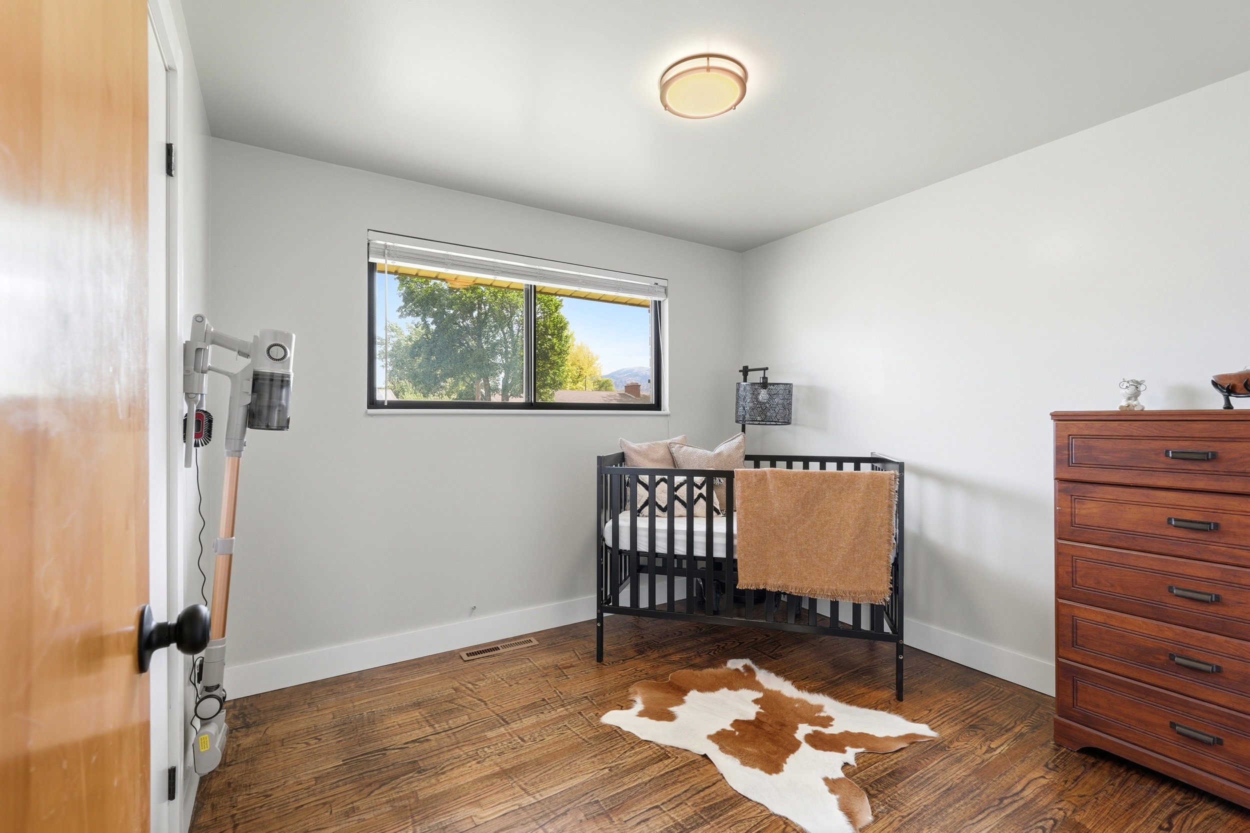 Bedroom featuring a single window with dark framing, wood-finish flooring, light-toned walls, white baseboards, and a flush-mount ceiling light fixture