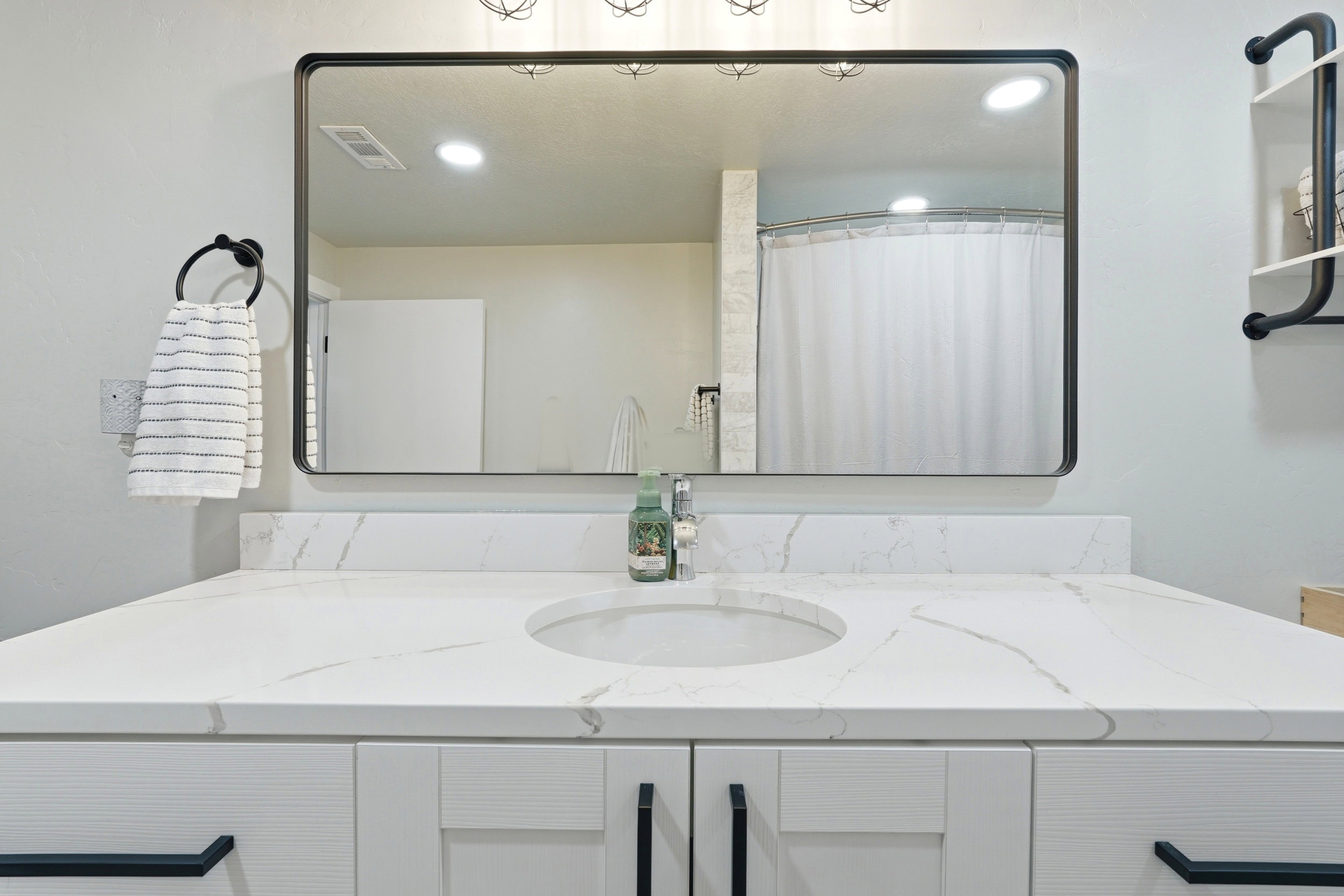 Bathroom vanity featuring an integrated sink, white countertop with subtle veining, white cabinetry with black hardware, and a framed rectangular mirror