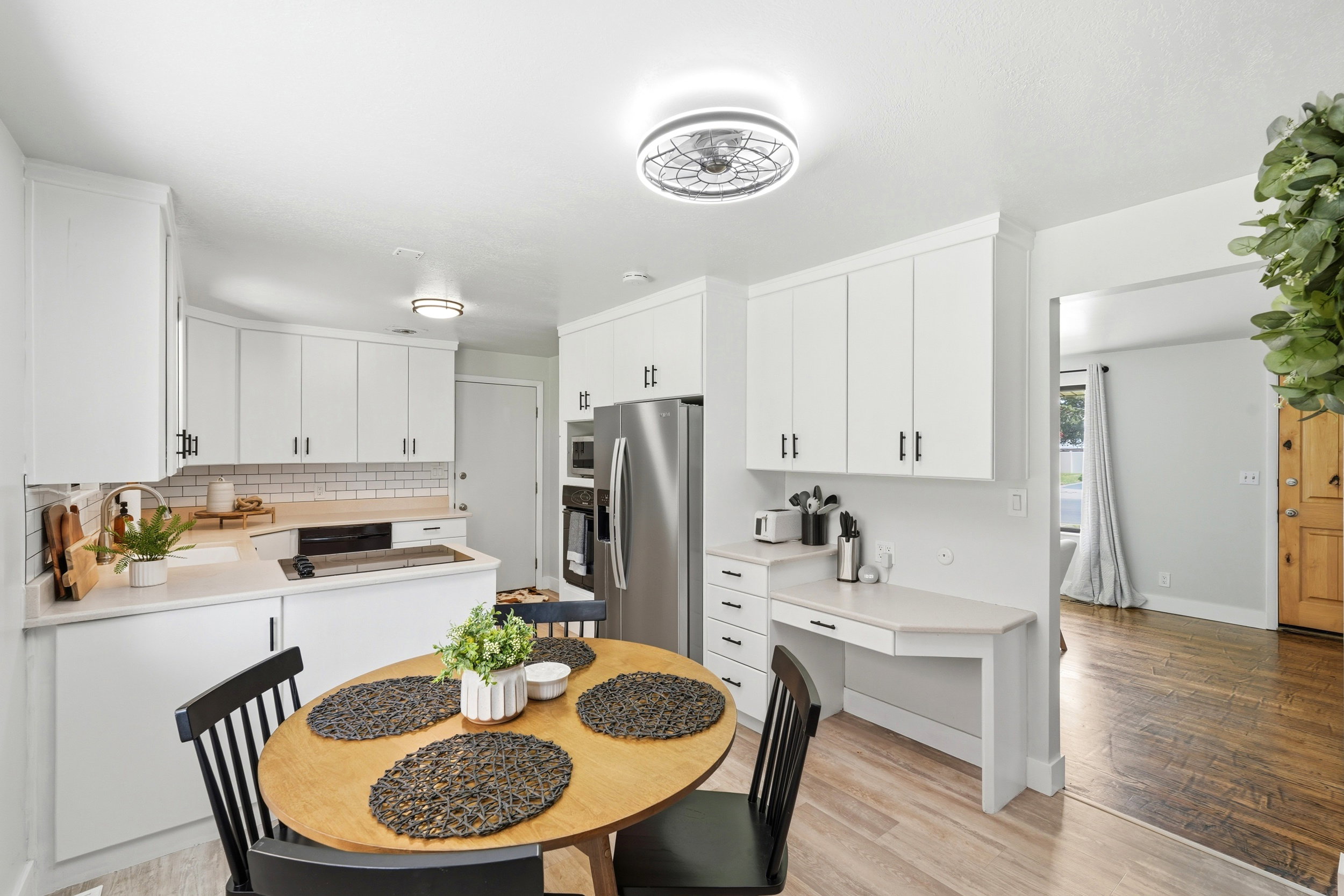 Kitchen featuring white shaker-style cabinetry, light wood-finish flooring, subway tile backsplash, and a built-in desk area