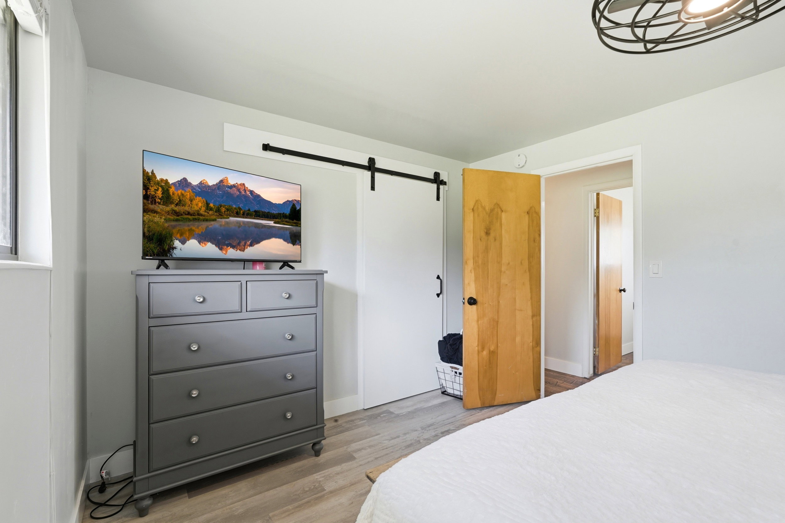 Bedroom featuring wood-finish flooring, light gray walls, a white barn door, and a natural wood interior door
